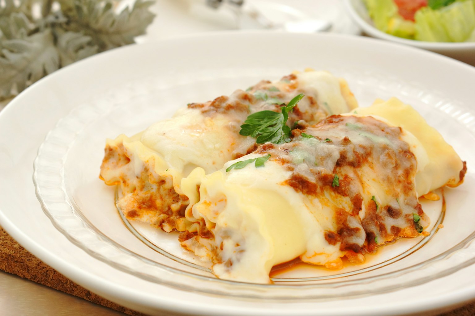 A plate of creamy cannelloni topped with meat sauce and cheese