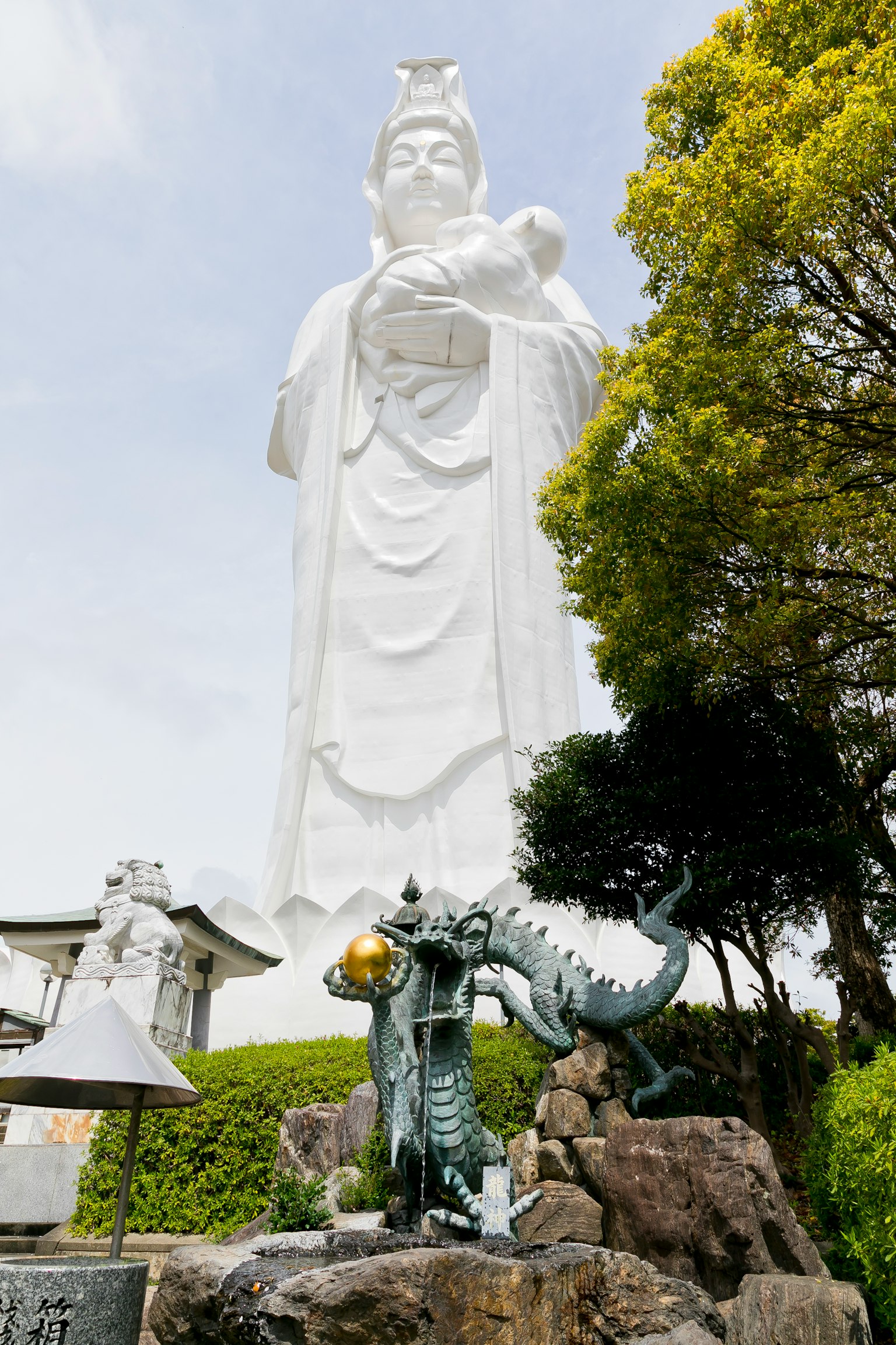 Una grande statua bianca di Kannon con una scultura di drago alla base