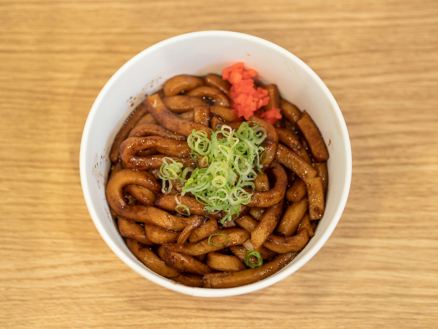 Noodles udon in un boccale bianco guarniti con cipollotti e zenzero marinato