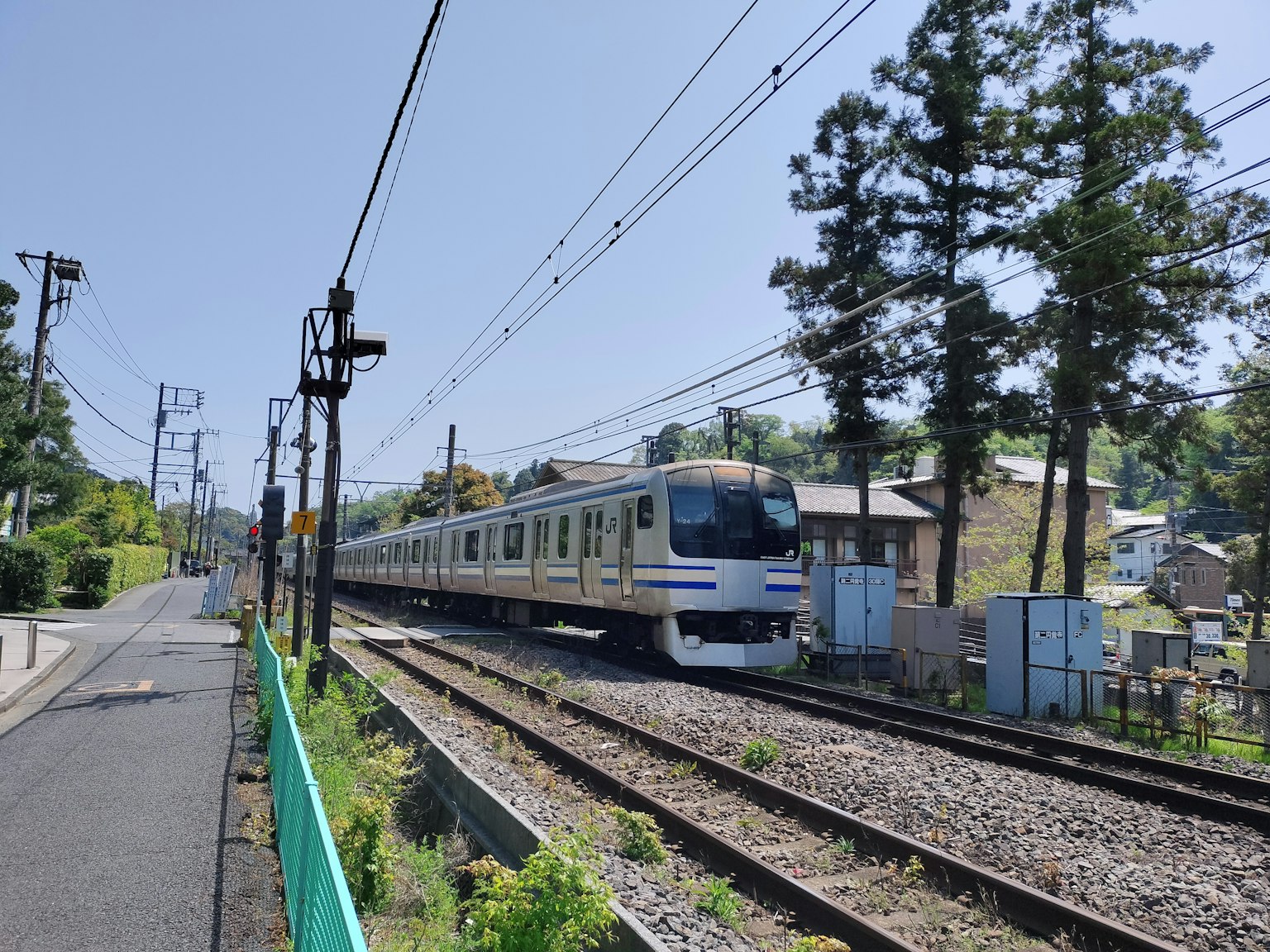 Treno in movimento sotto un cielo blu con alberi e edifici circostanti