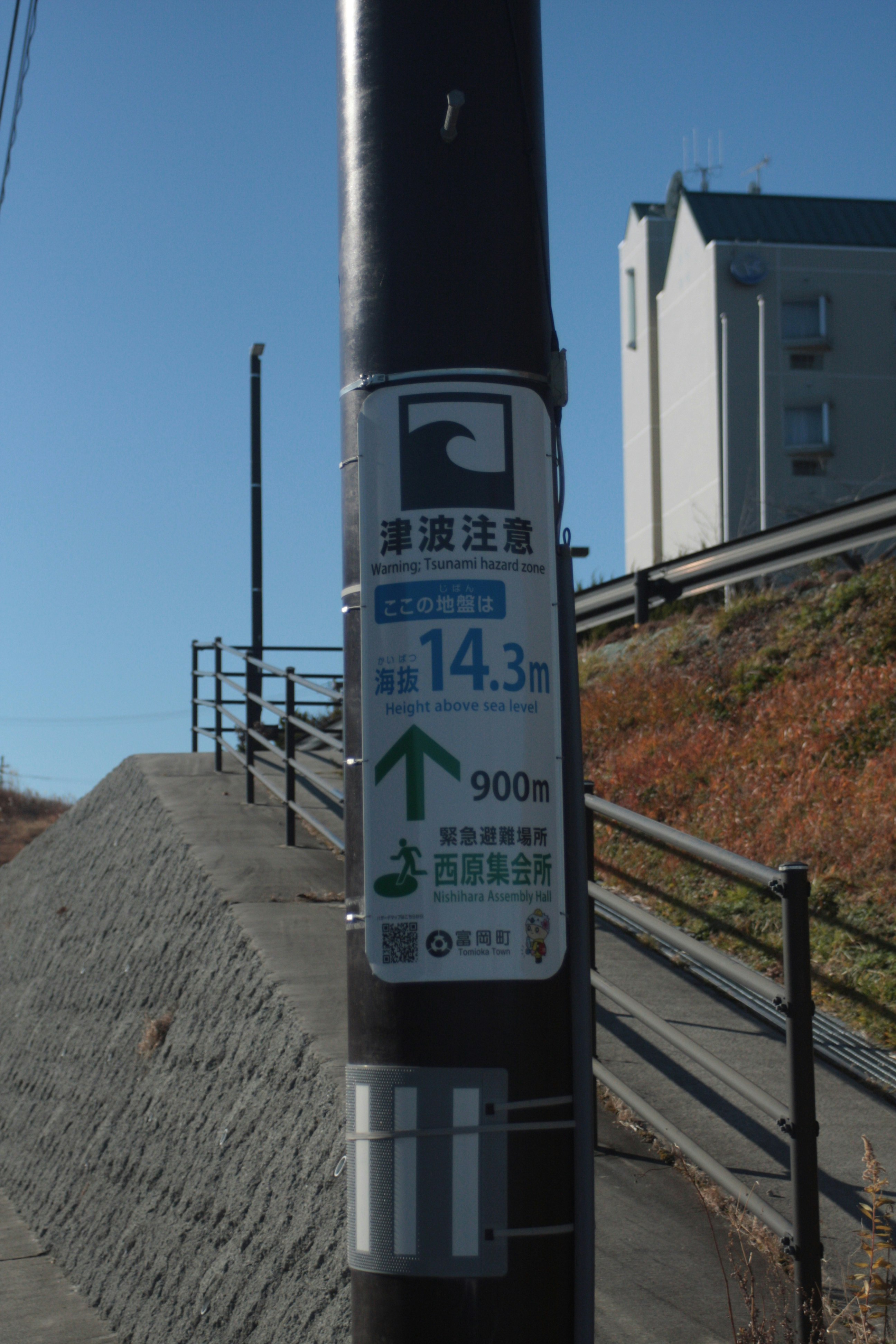 Warnschild vor Tsunamis neben einer Küstenböschung