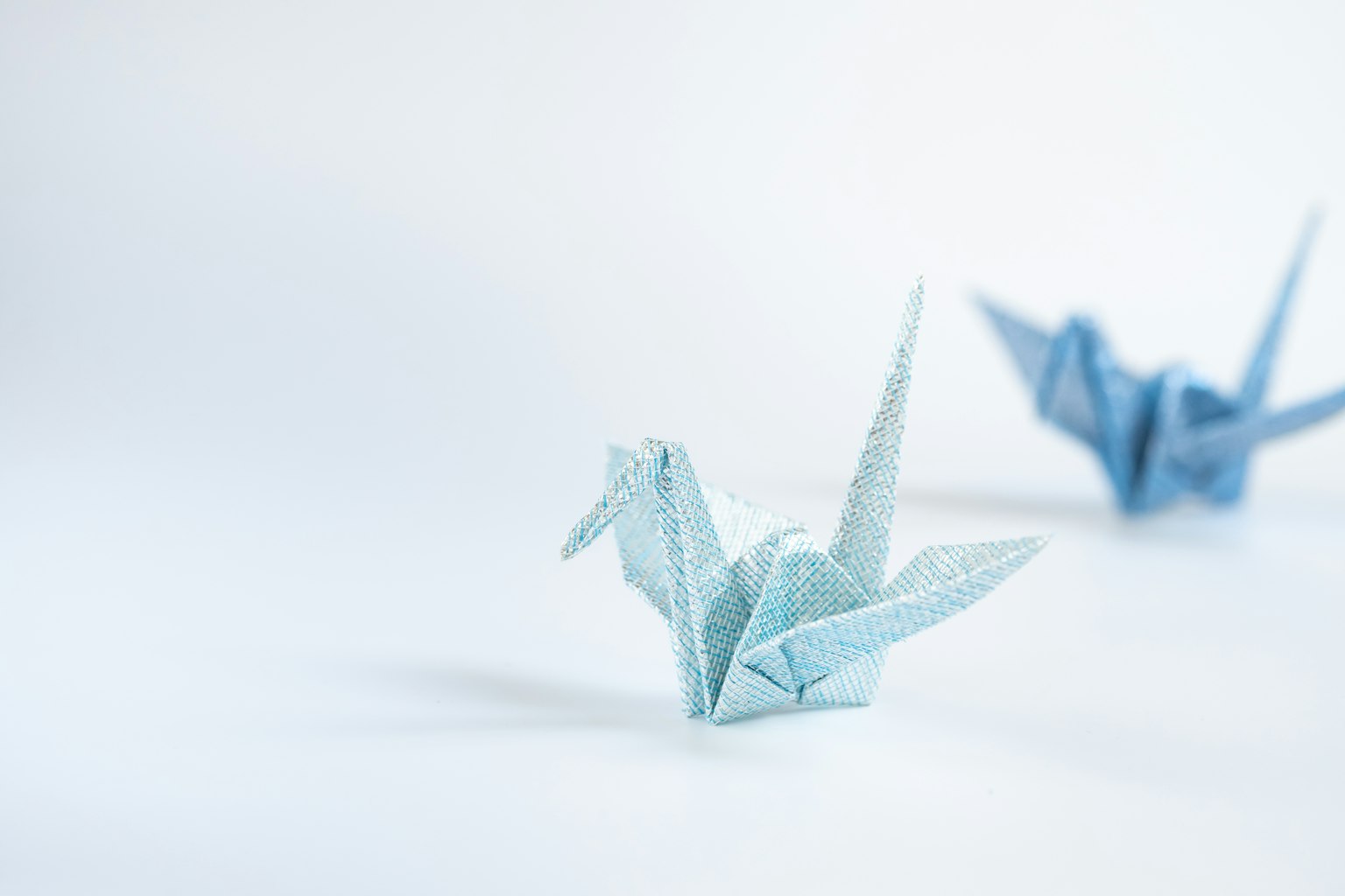 Gru in origami blu chiaro in primo piano con un'altra gru sfocata sullo sfondo