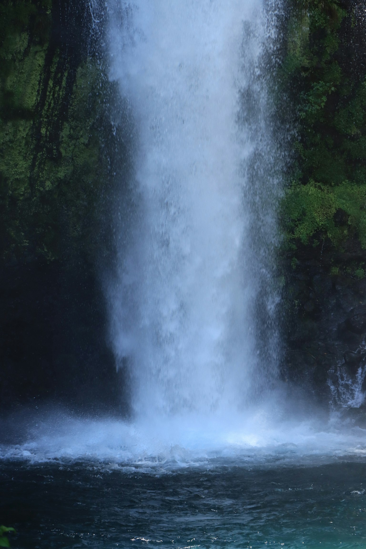 Pemandangan indah air terjun yang mengalir di atas batuan dikelilingi lumut hijau