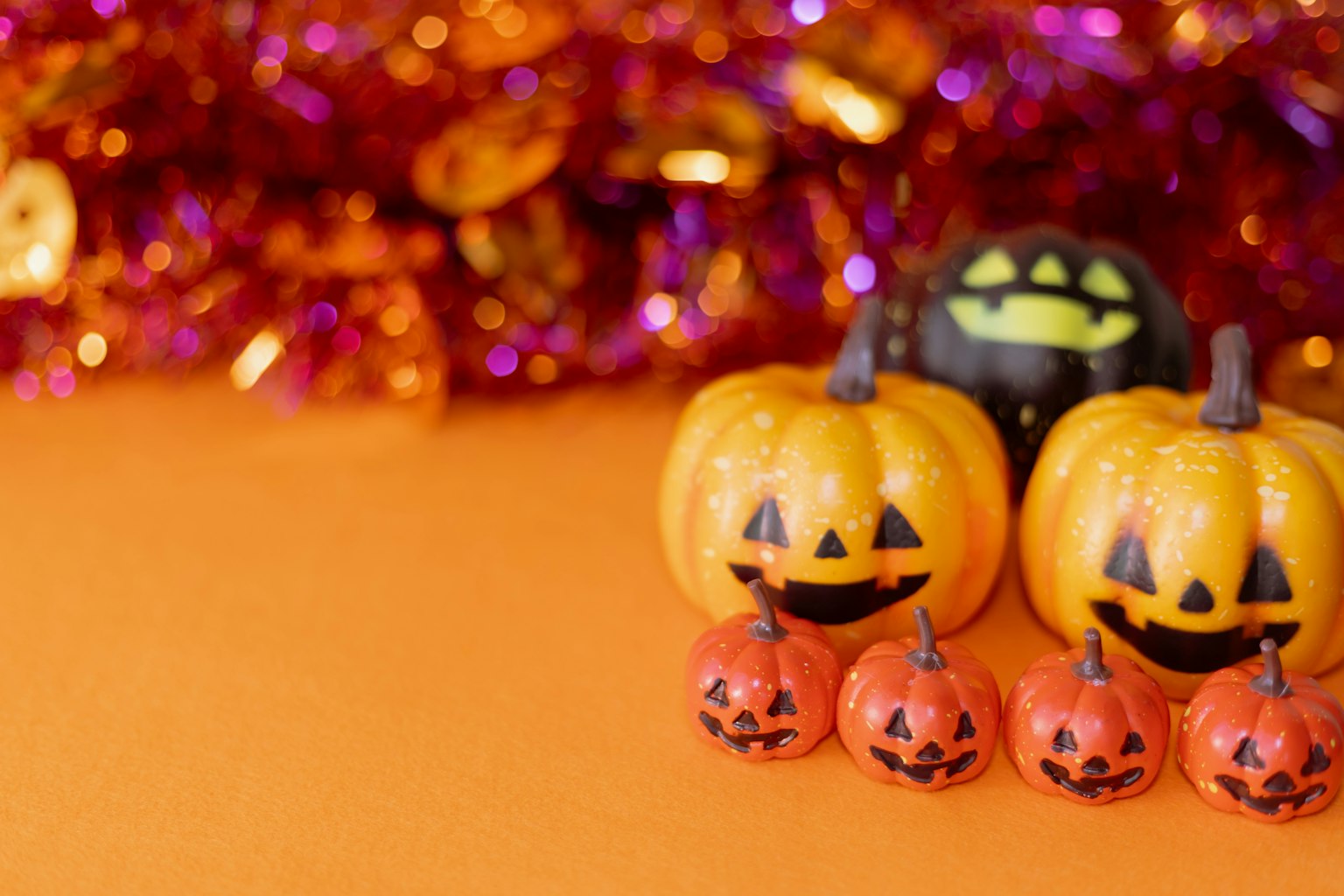 Zucche con facce di jack-o'-lantern disposte su uno sfondo arancione con festoni colorati sullo sfondo