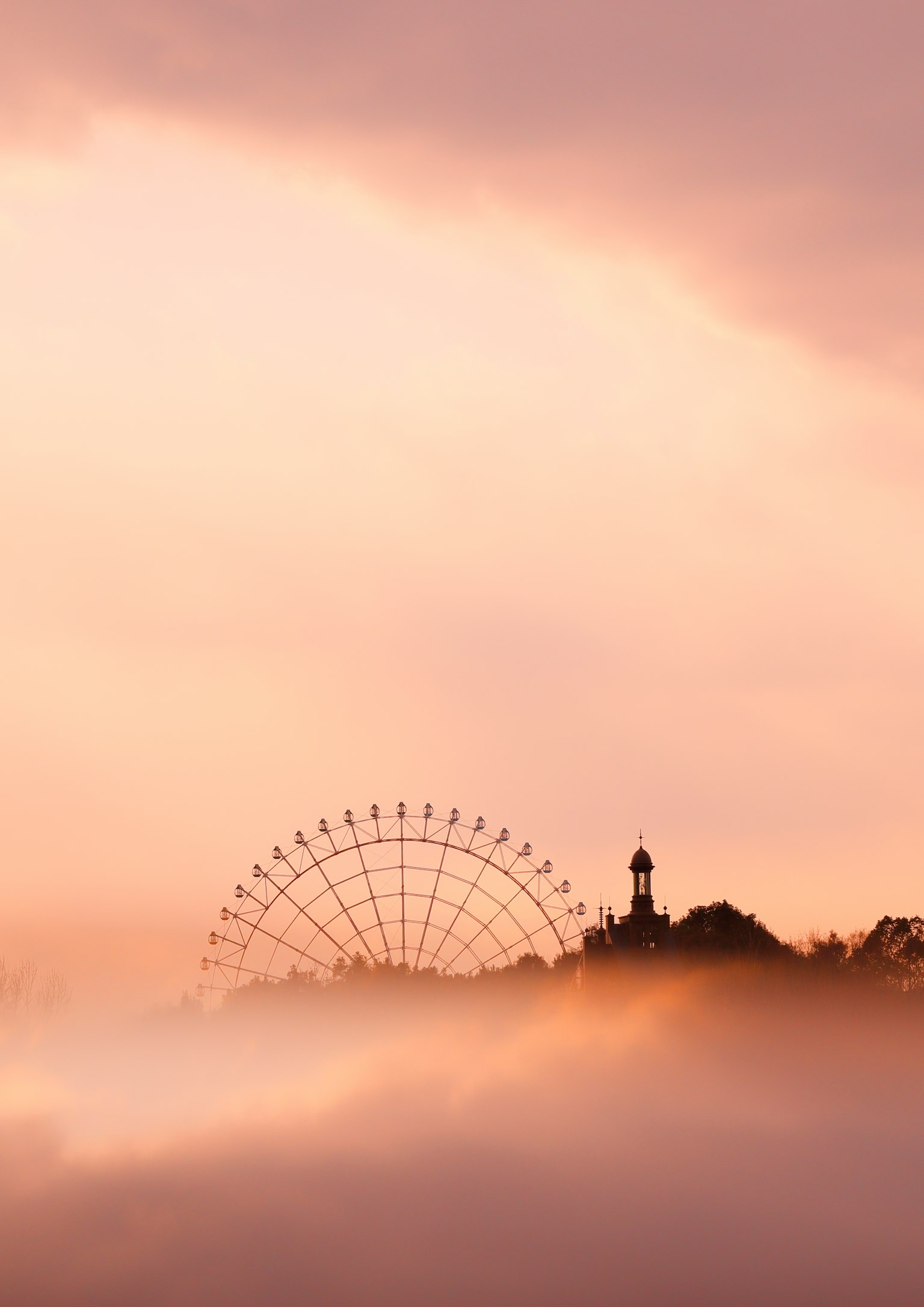 Silhouette d'une grande roue et d'une tour émergeant de la brume avec un ciel rose