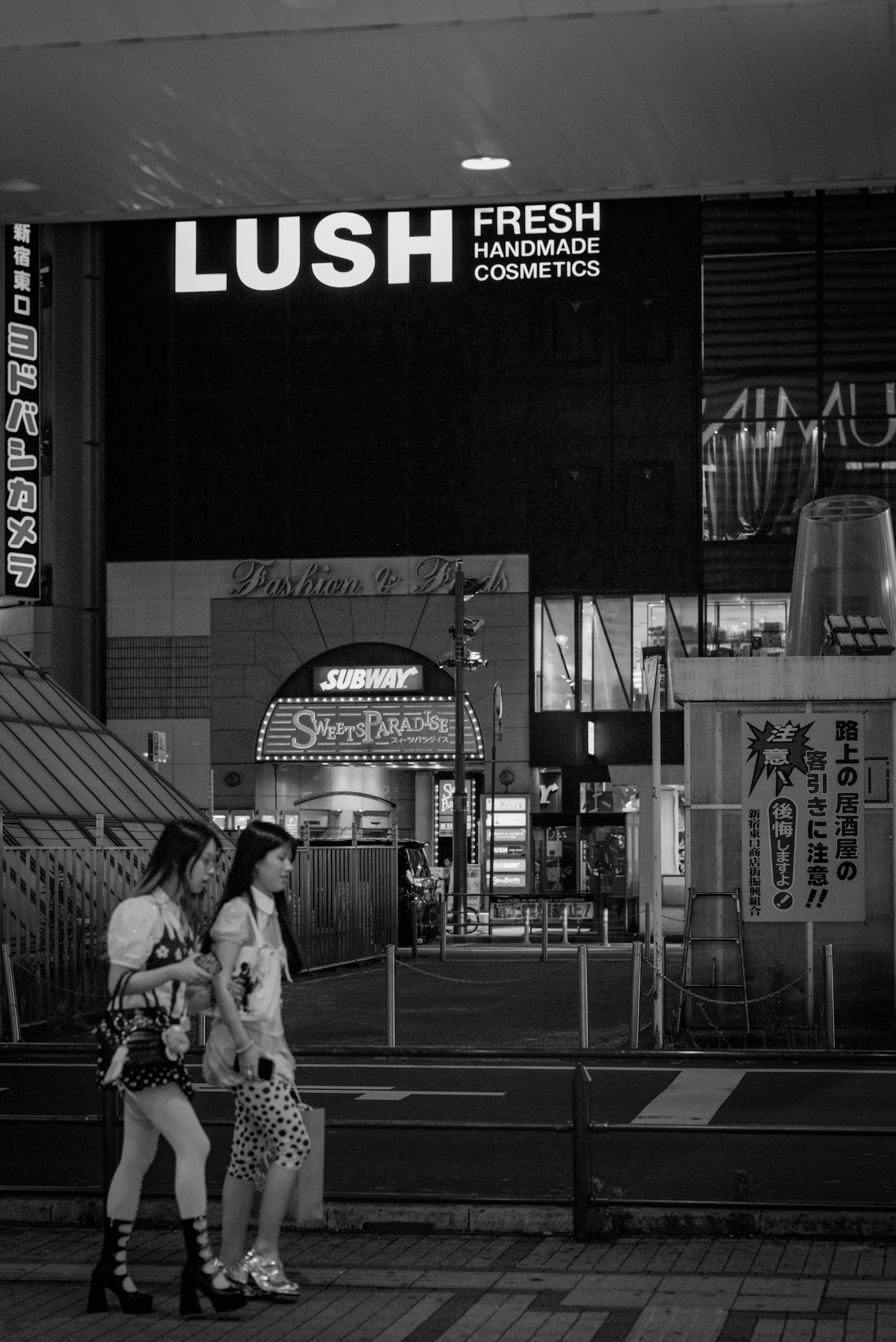 两名女性在城市环境中夜晚走在LUSH商店前
