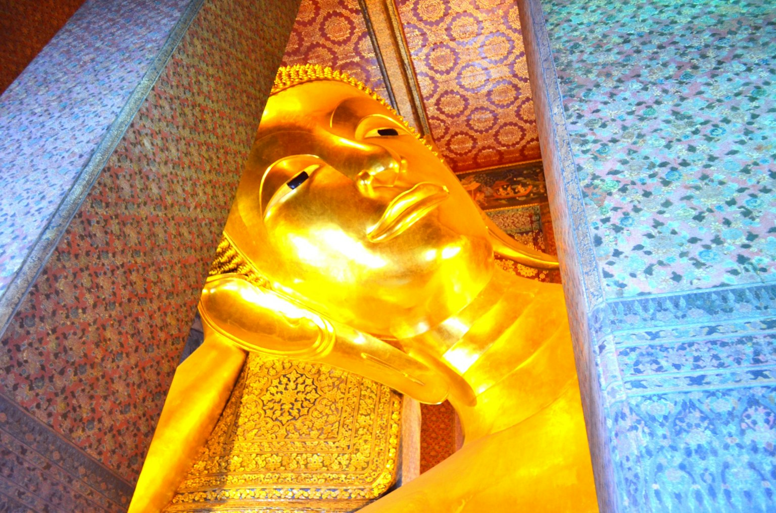 Golden reclining Buddha statue's face visible with decorative background