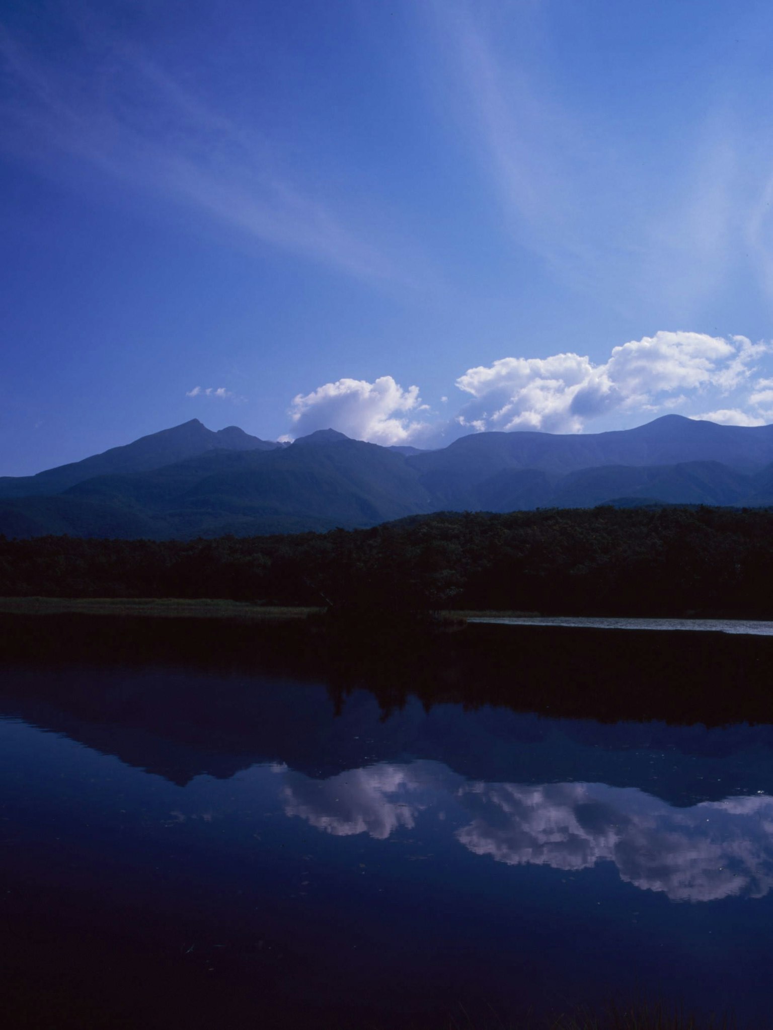 Lac serein reflétant le ciel bleu et les nuages avec des montagnes en arrière-plan mettant en valeur la beauté naturelle