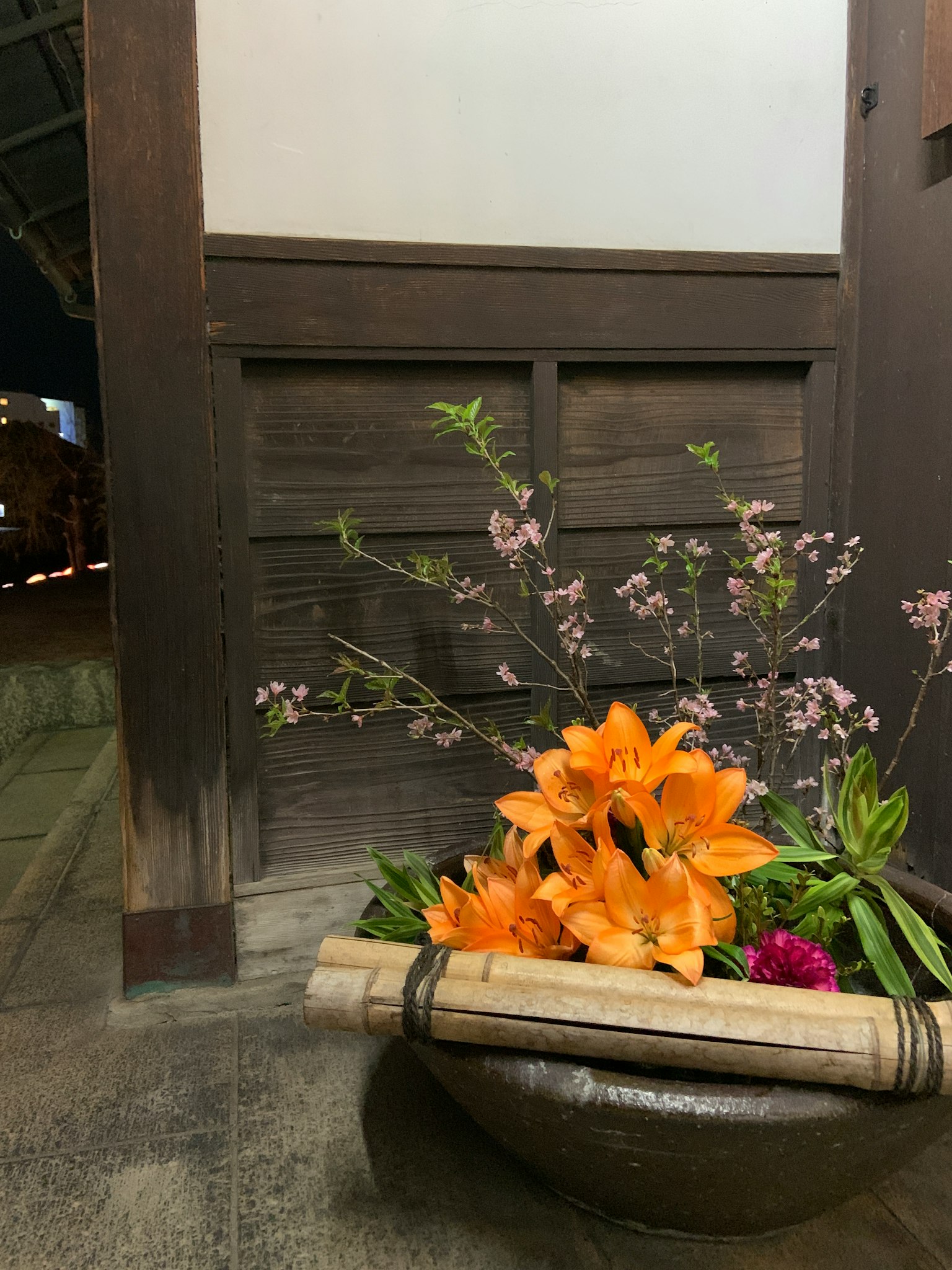 Traditional flower arrangement with orange lilies and cherry blossoms in a hallway
