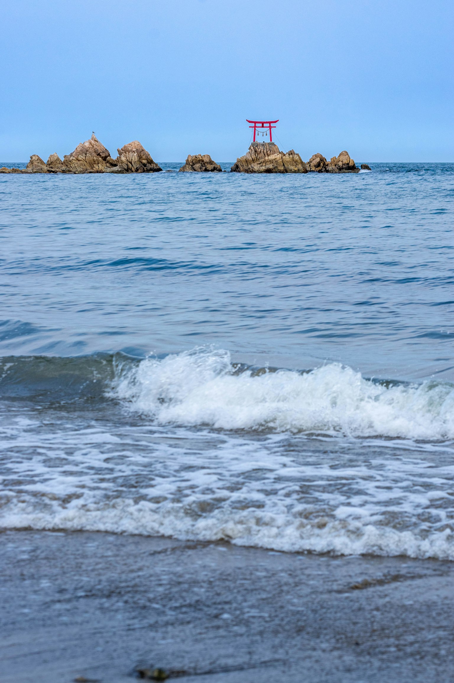 Vista panoramica di rocce costiere e un cancello torii rosso nell'oceano