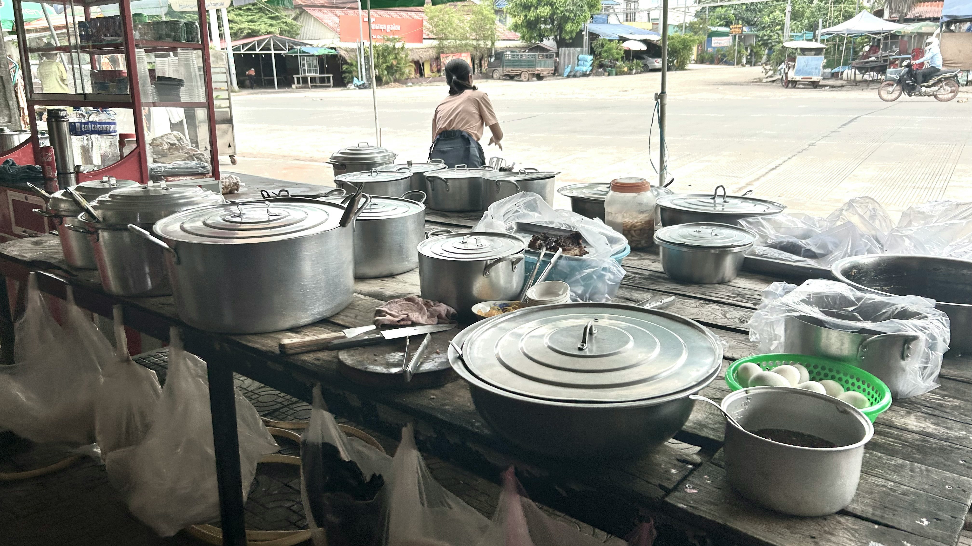 屋外の屋台で鍋や食器が並ぶ調理風景