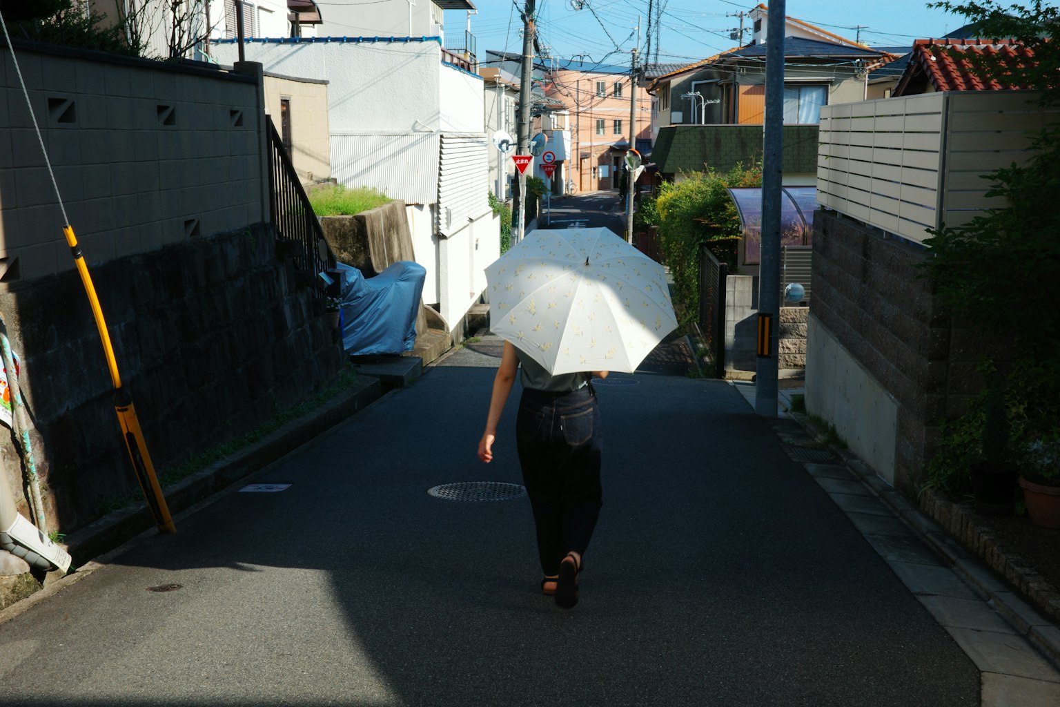 흰 우산을 들고 좁은 골목을 걷는 여성