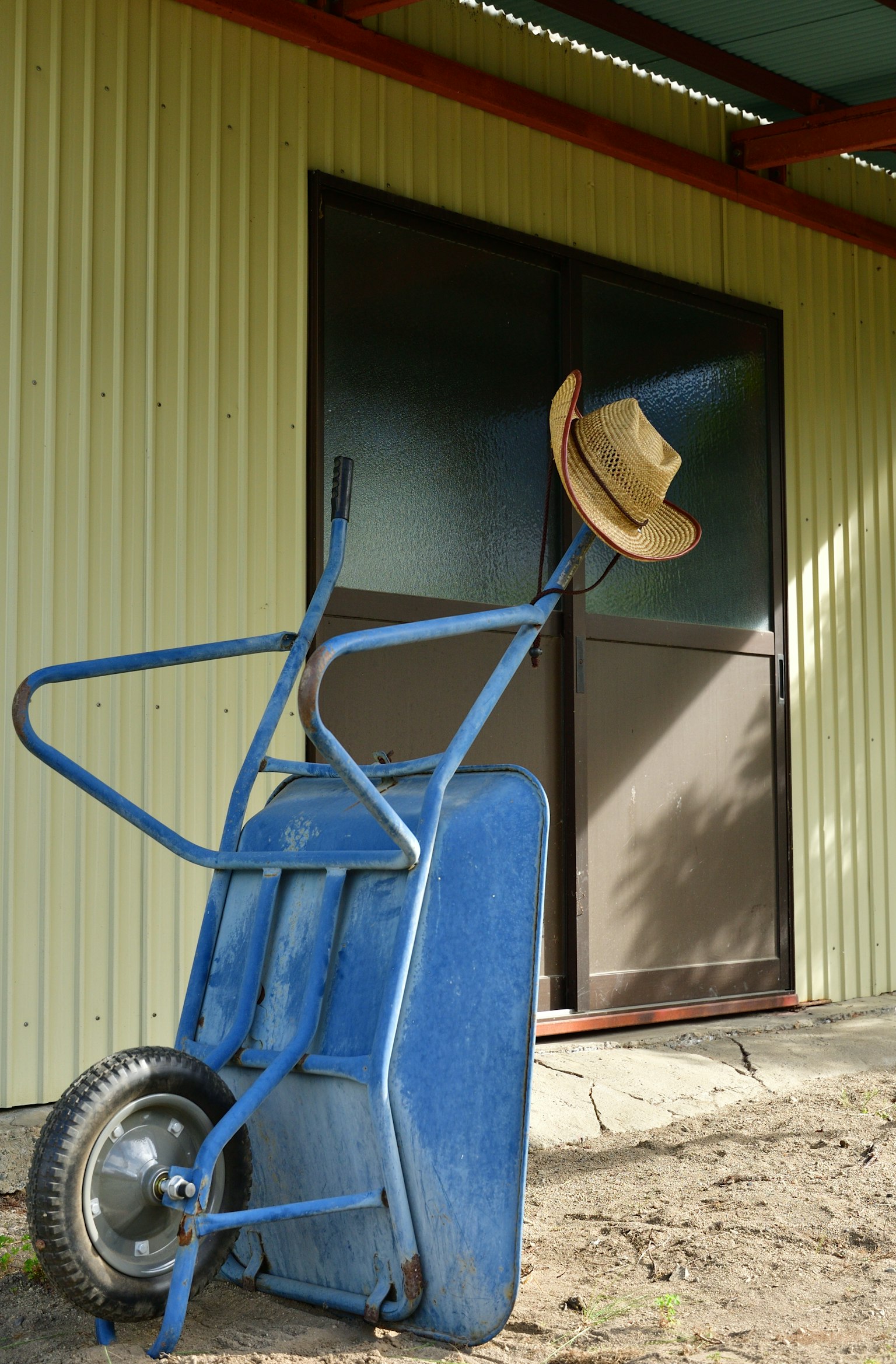 Blue wheelbarrow with a straw hat leaning against a building