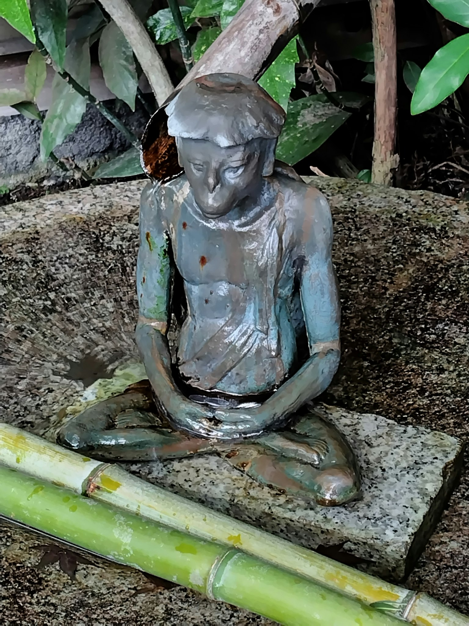 青铜坐像位于石基上，周围环绕着绿色植物