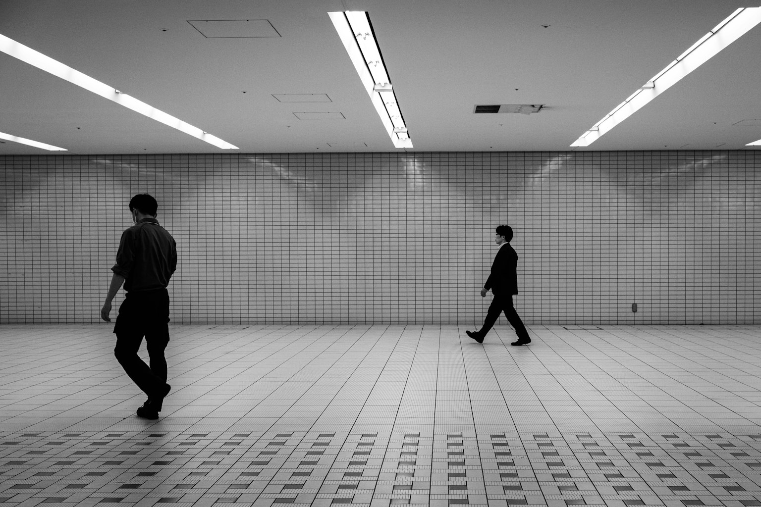 白黒の地下道を歩く二人の男性が映るシンプルな構図の画像
