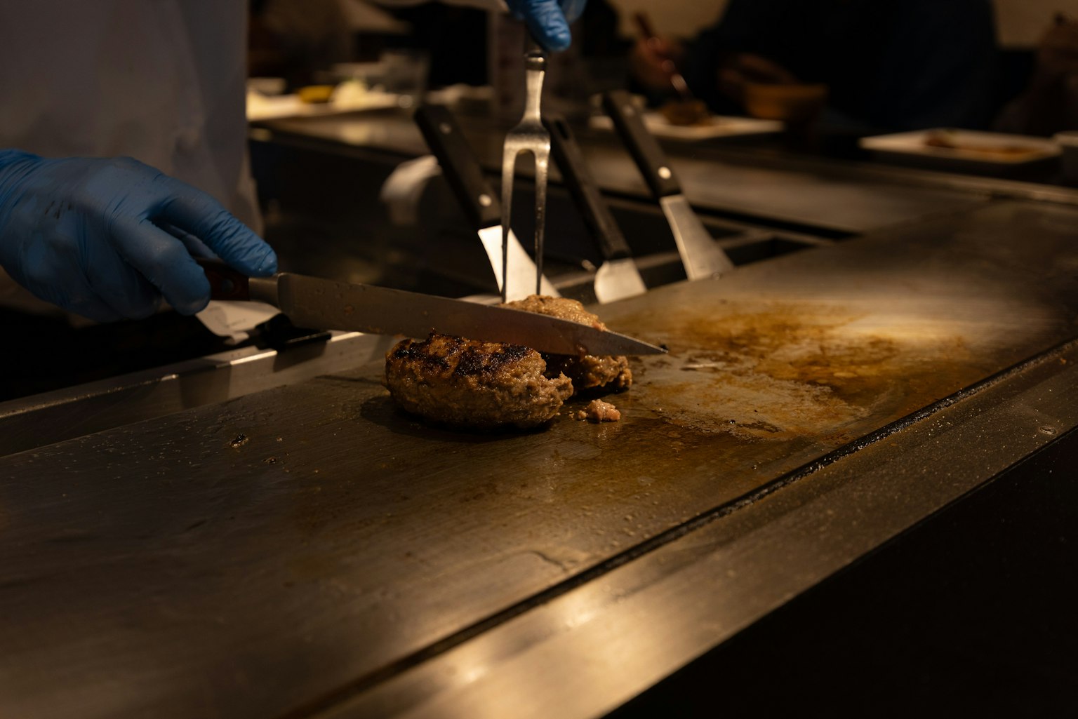 穿著藍色手套的廚師在鐵板上切割食物