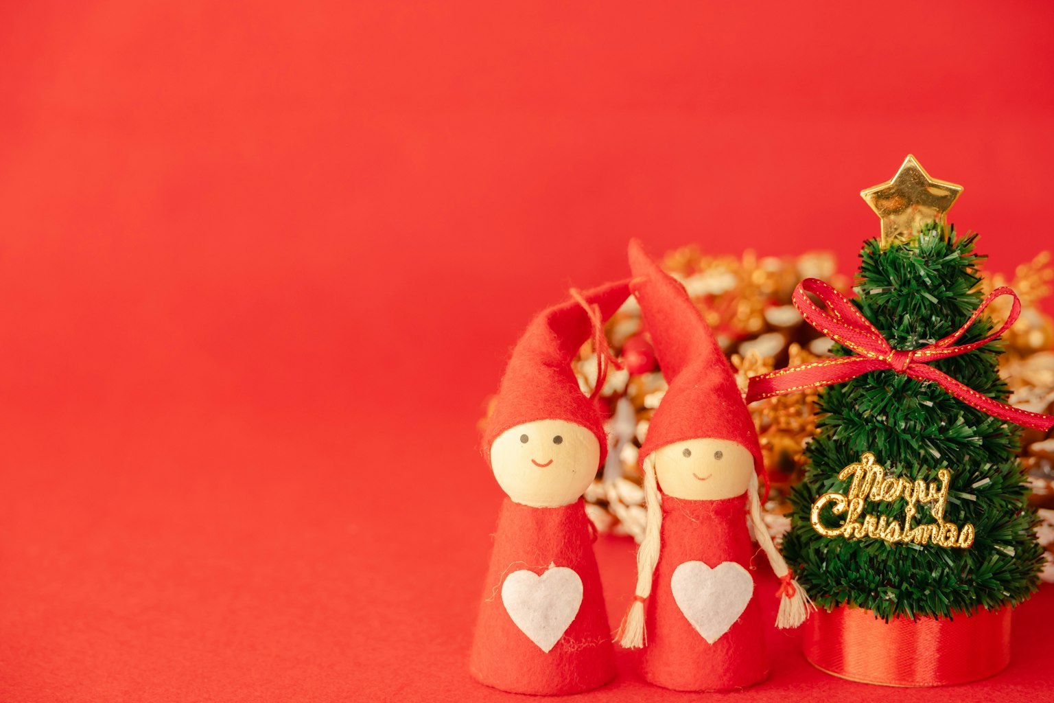 Due figure natalizie in abiti rossi con cuori accanto a un piccolo albero di Natale