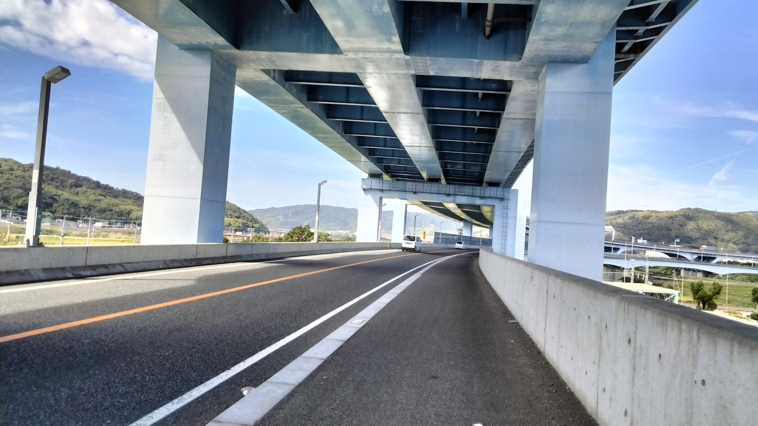 View under an elevated highway featuring concrete pillars and a curved road