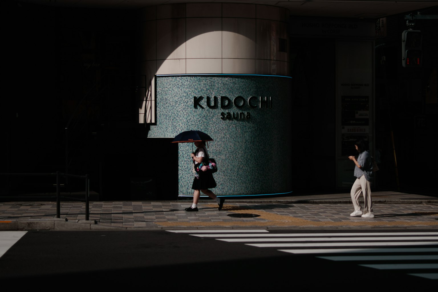 一位女性在昏暗的街道上走，手持雨傘，背景是KUDOKU標誌