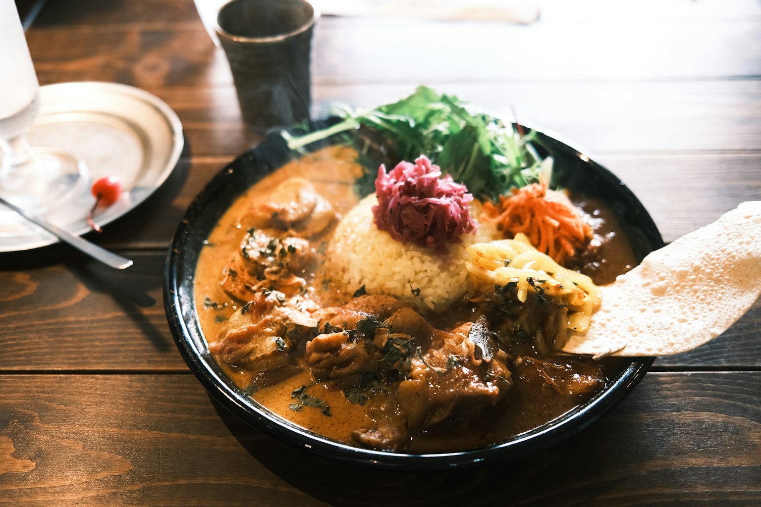 Un plato con curry cremoso y arroz cubierto con verduras frescas y un trozo de pan