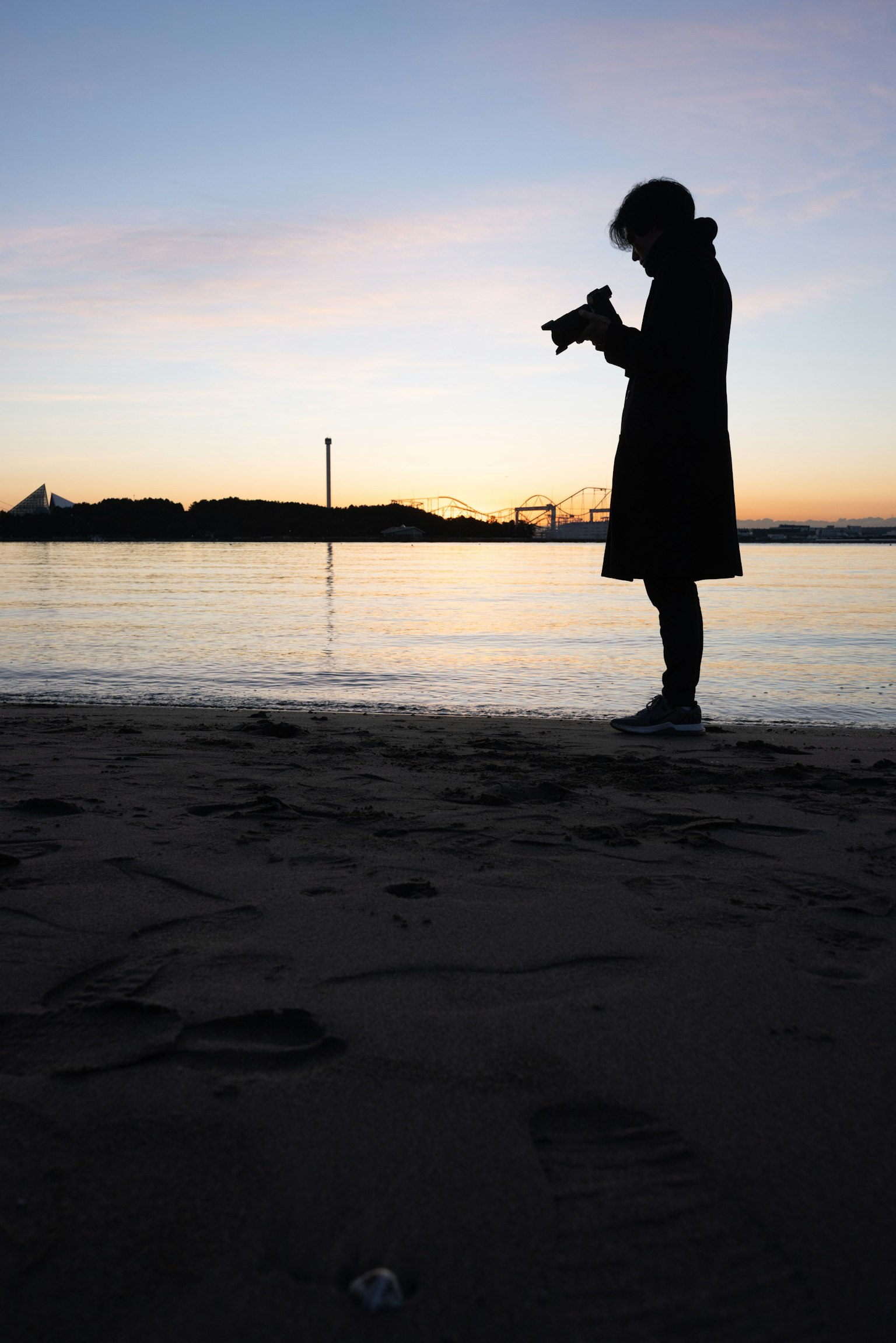 Silueta de una persona sosteniendo una cámara en la playa durante el atardecer