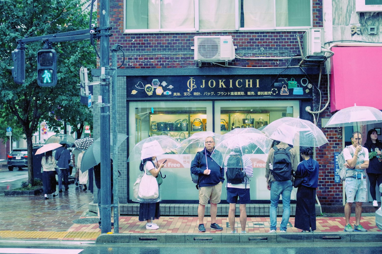 Persone in attesa con ombrelli in una giornata di pioggia davanti al negozio JOKICHI