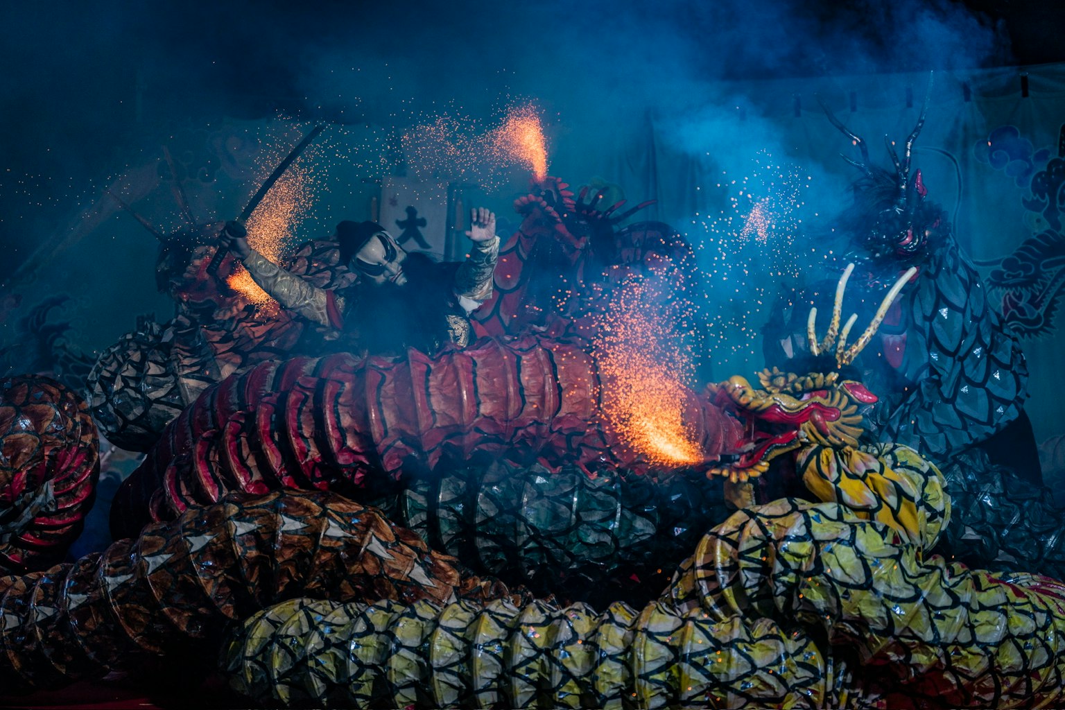 色とりどりのドラゴンの衣装を着たパフォーマーが煙の中で踊る祭りのシーン
