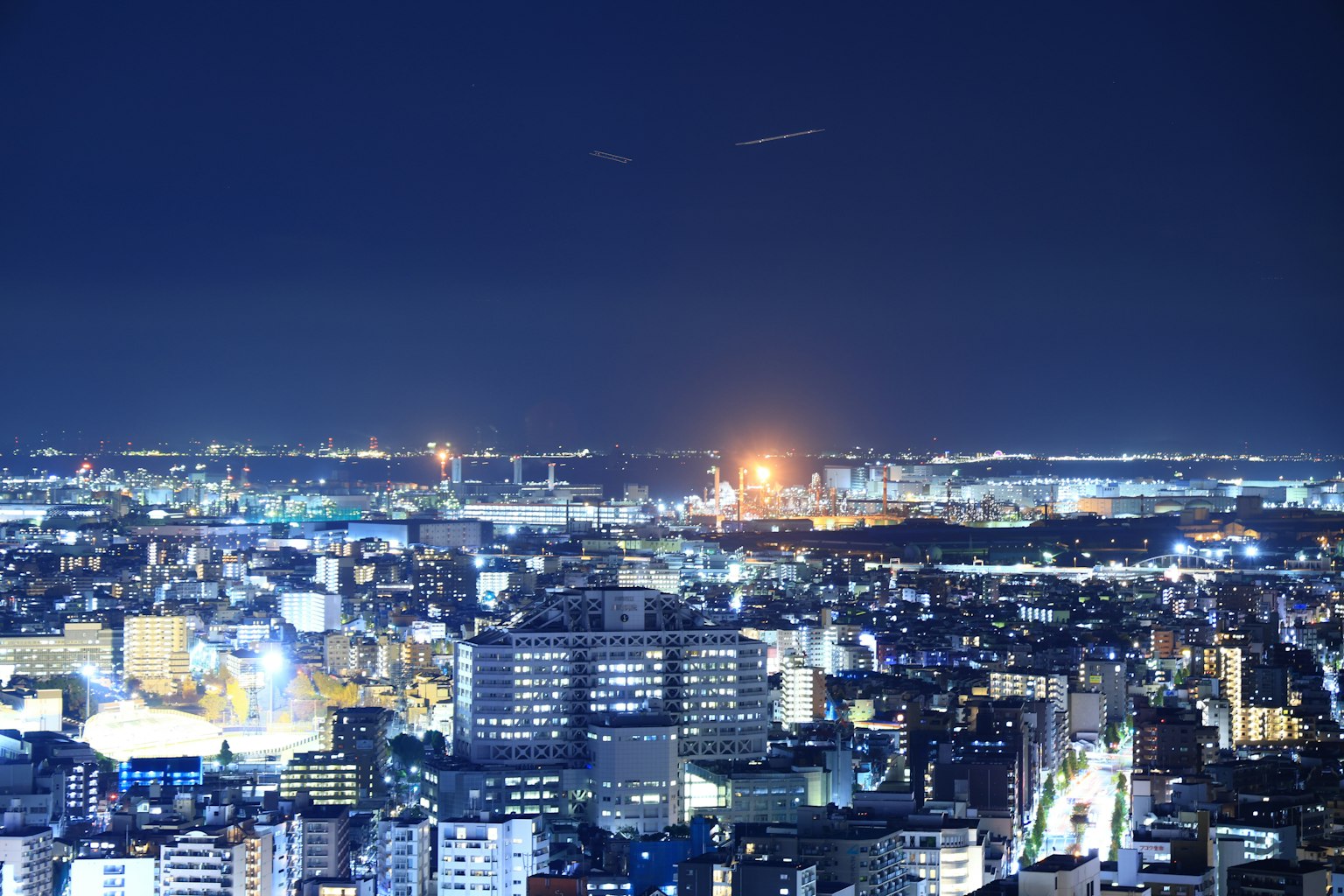 Panoramablick auf eine Stadt bei Nacht mit hellen Gebäuden und Straßenlaternen entfernte leuchtende Fabriken