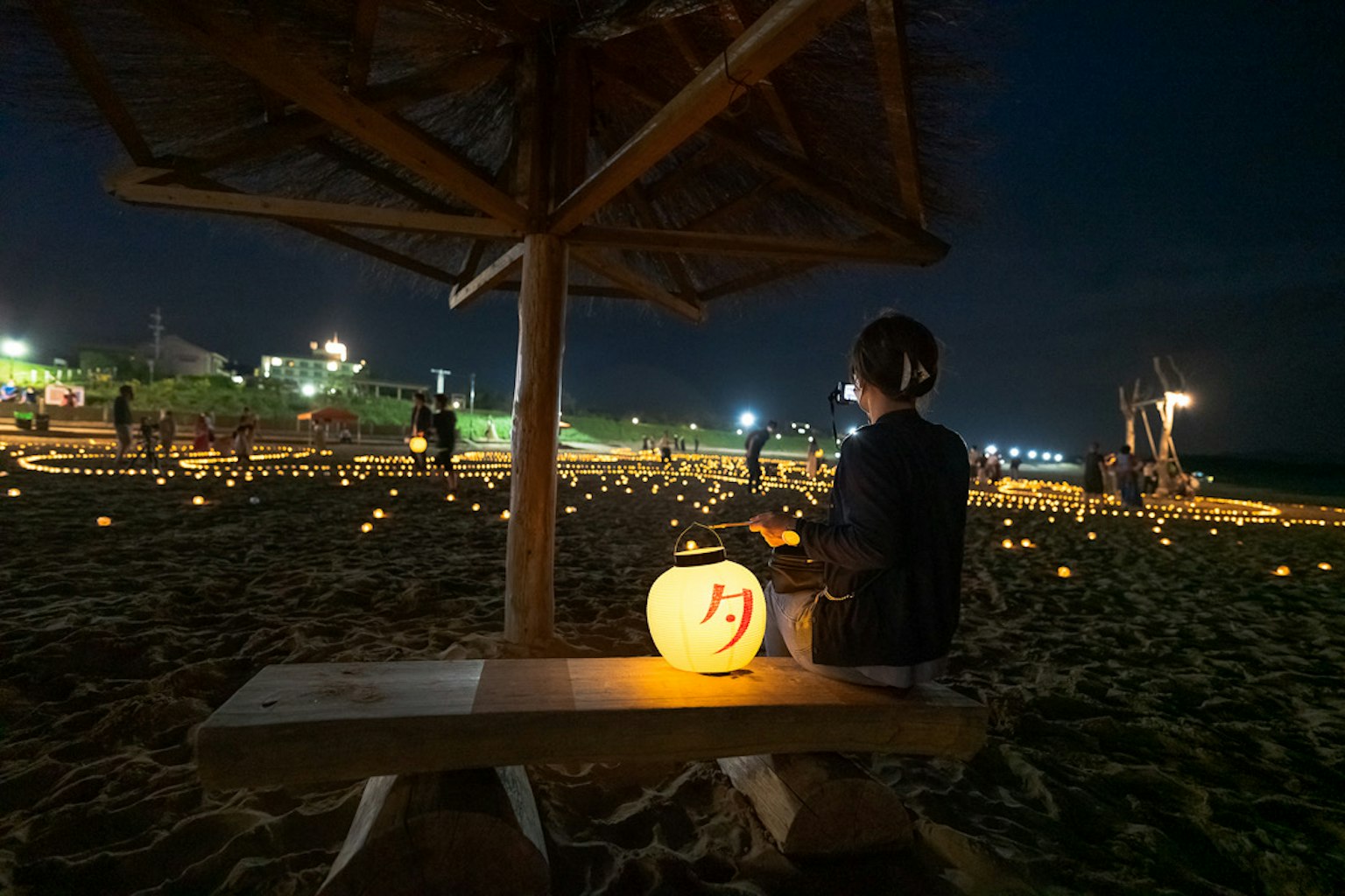 夜晚海灘上，一個人手持燈籠，周圍是蠟燭