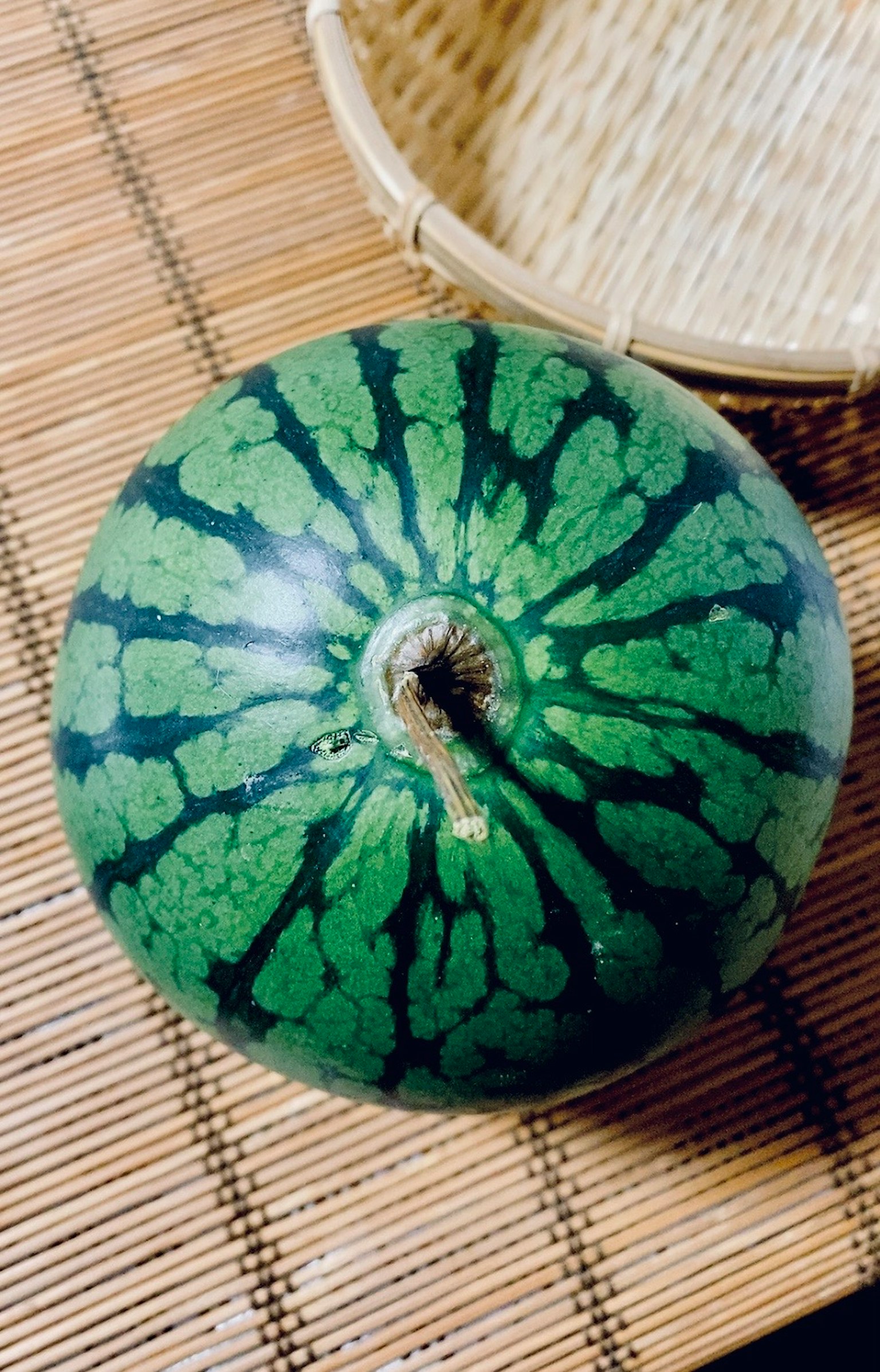 Una sandía verde vibrante colocada sobre una estera de bambú