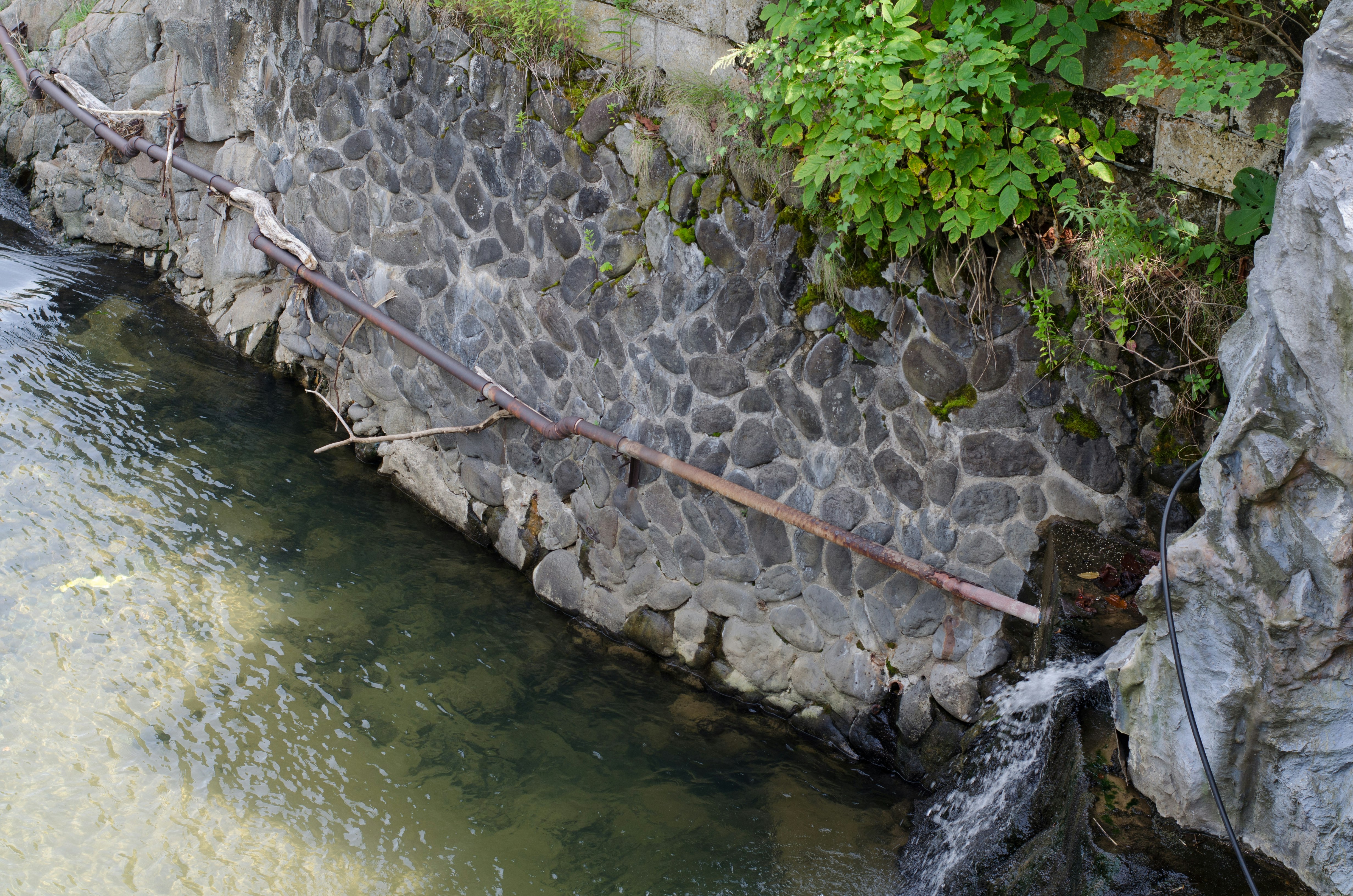 ruisseau bordé de pierres avec une barrière métallique et petite cascade