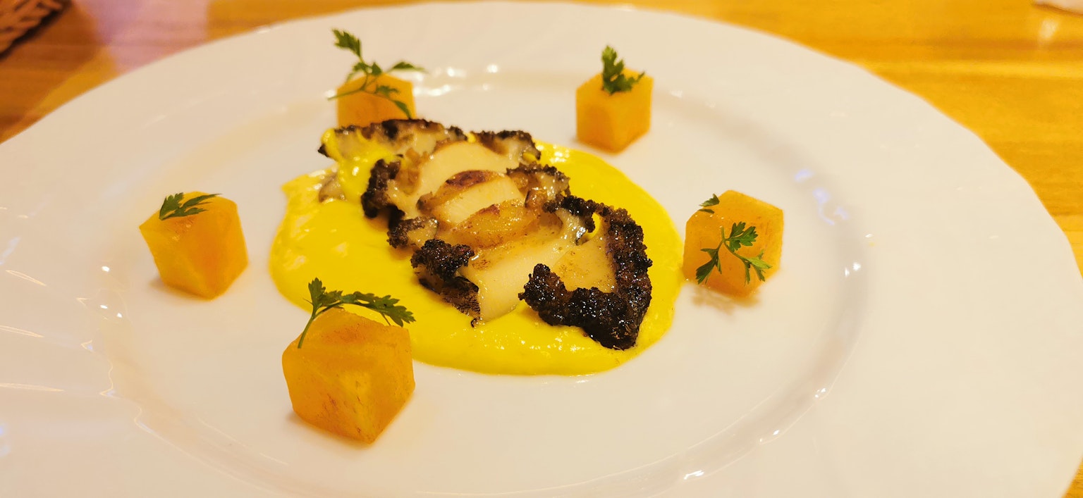 Ikan panggang di piring putih dengan saus kuning dikelilingi oleh sayuran berbentuk kubus oranye