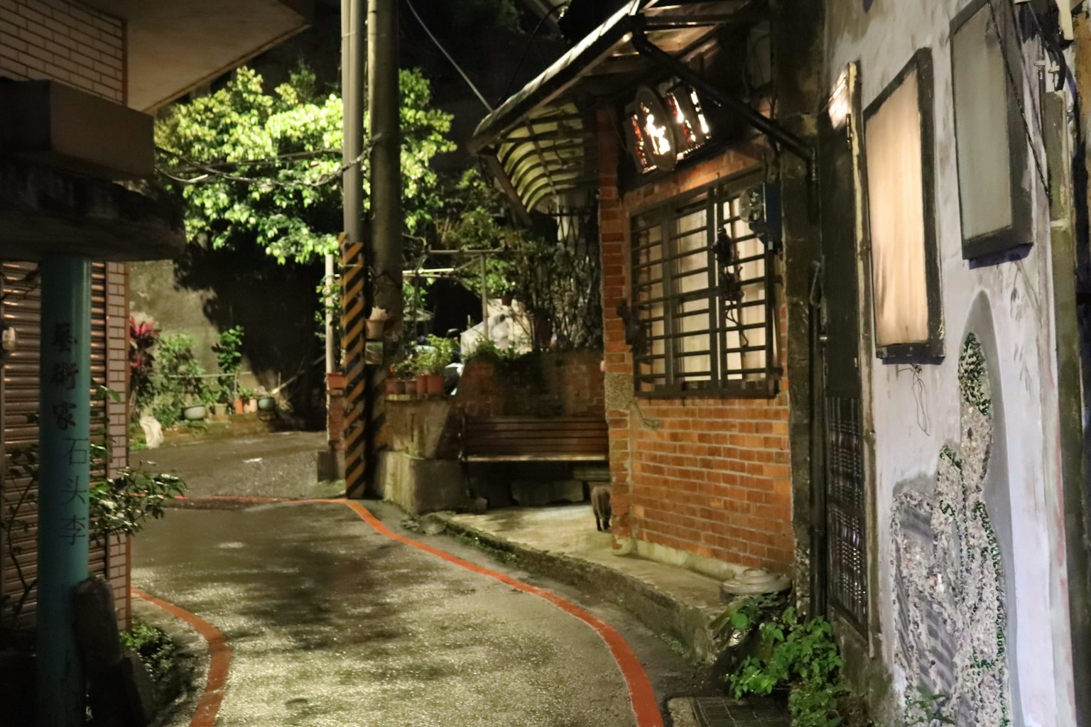 Gang sempit dengan rumah bata tua dan tanaman hijau di malam hari