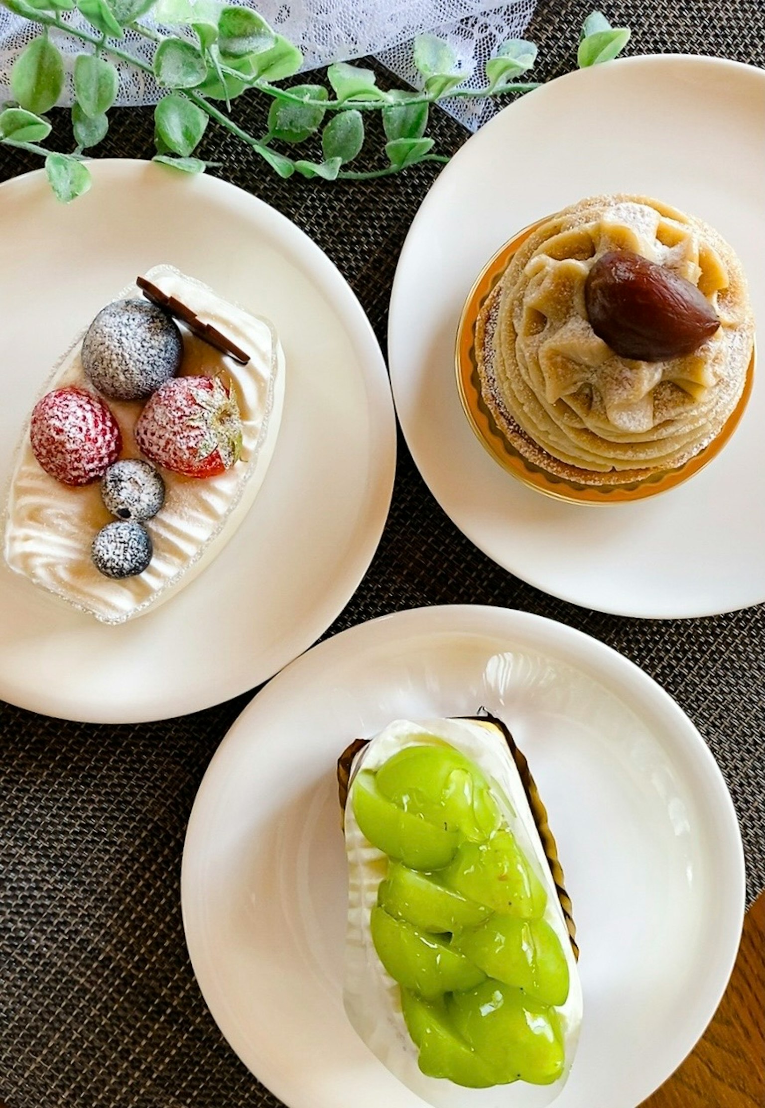 三种不同的甜点摆放在白色盘子上,特色是水果装饰的蛋糕和栗子奶油甜点