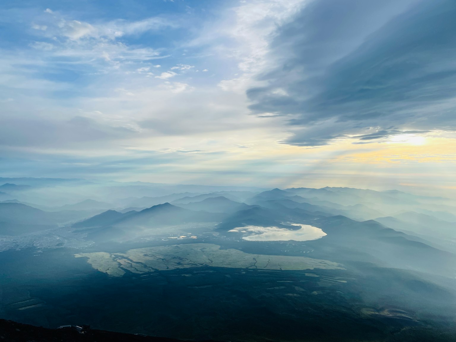 Paysage majestueux depuis le sommet d'une montagne avec des montagnes brumeuses et un ciel bleu montrant un lac au centre