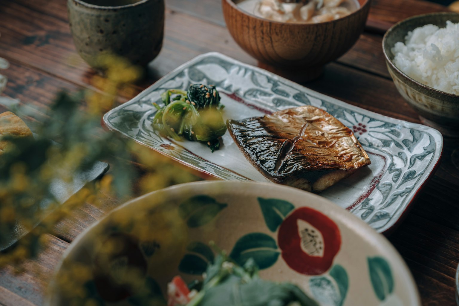 Un plato bellamente dispuesto de pescado a la parrilla con verduras frescas en una mesa de comedor japonesa