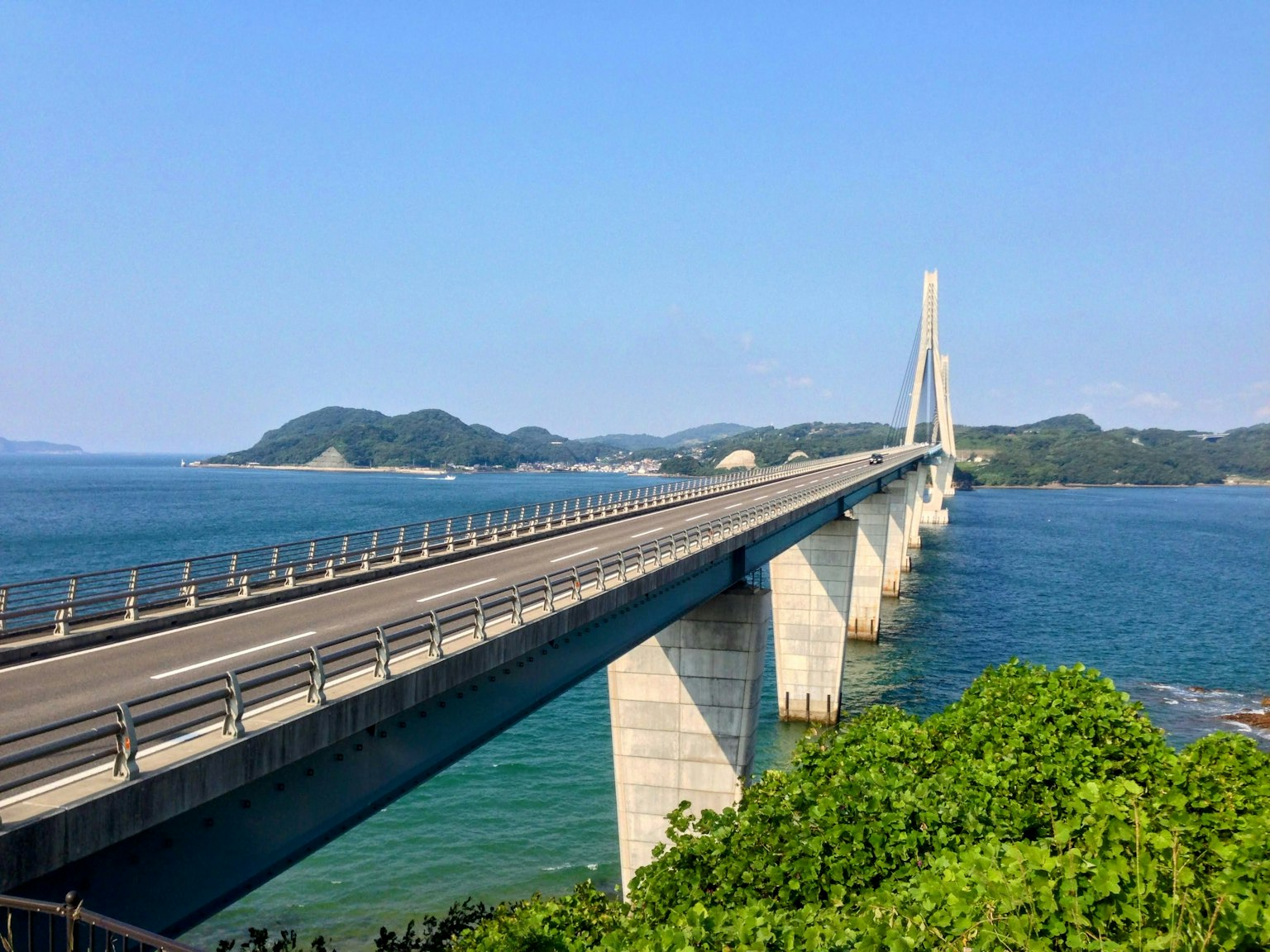 สะพานยาวข้ามทะเลสีน้ำเงินพร้อมใบไม้สีเขียว