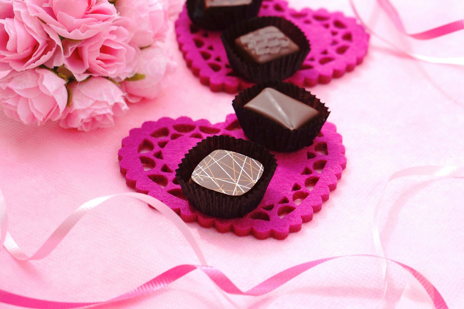 粉色背景上心形蕾絲墊上排列的美麗巧克力和粉色玫瑰