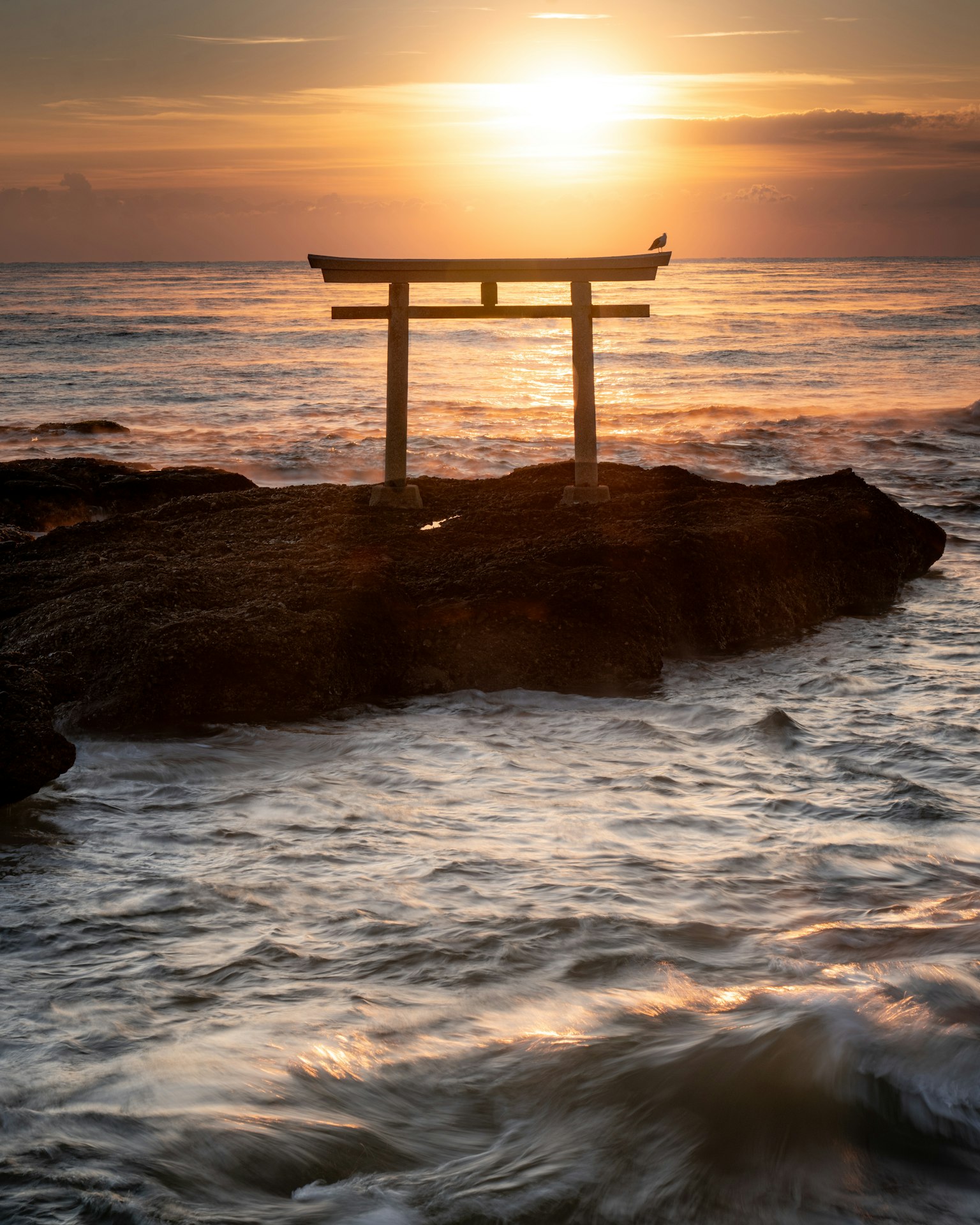 Torii en silueta contra un atardecer sobre el océano