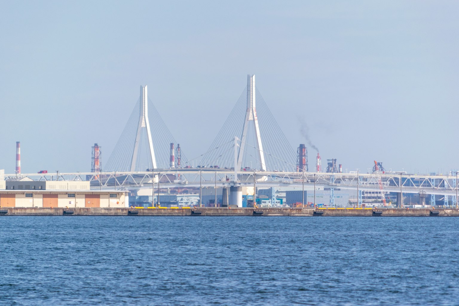 Jembatan modern menjulang di atas laut dengan pemandangan pelabuhan