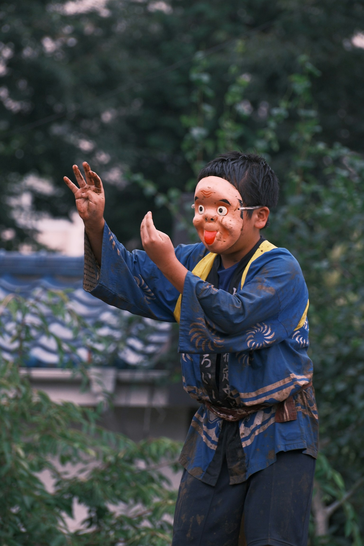 Seorang anak laki-laki dalam pakaian tradisional Jepang melakukan pertunjukan dengan topeng