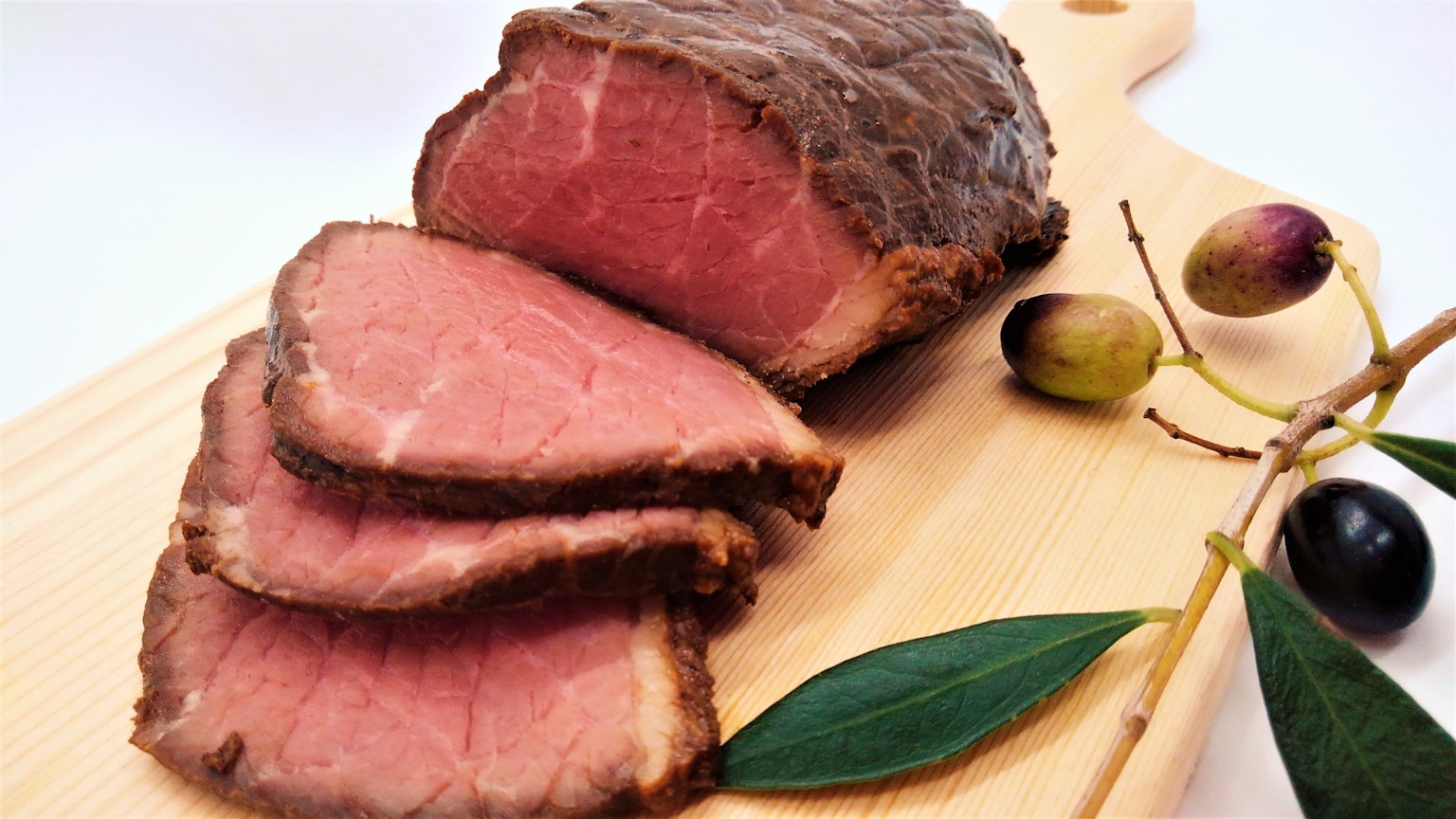 Sliced roast beef with olive branches on a wooden cutting board