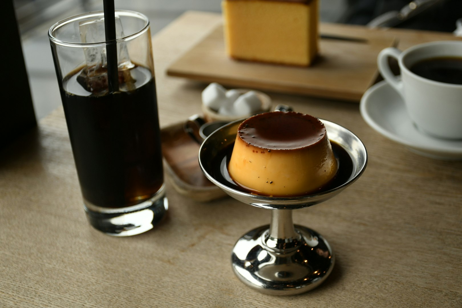コーヒーカップとプリン、グラスが並ぶカフェのテーブル