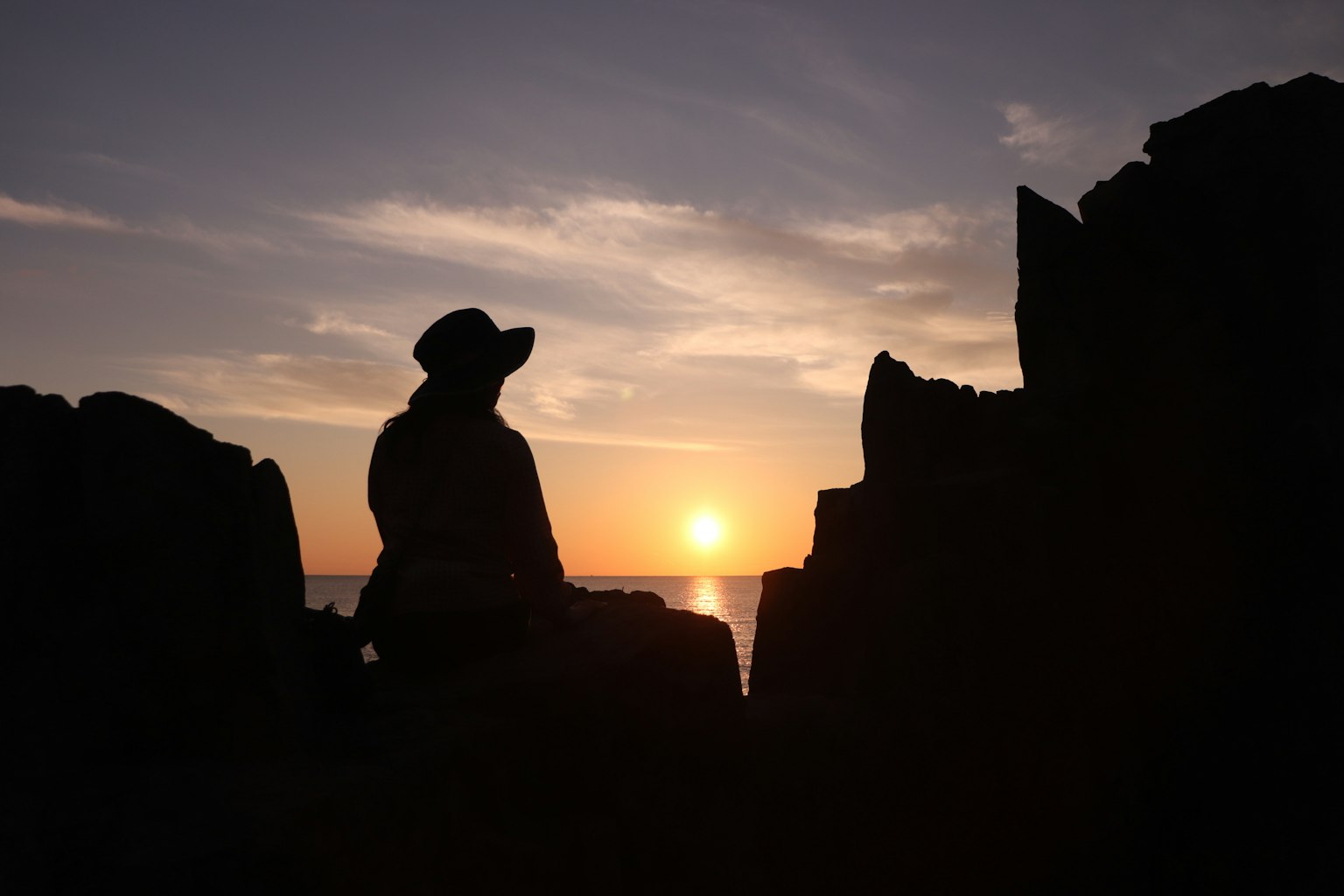 Silhouette of a person sitting between rocks with a sunset in the background