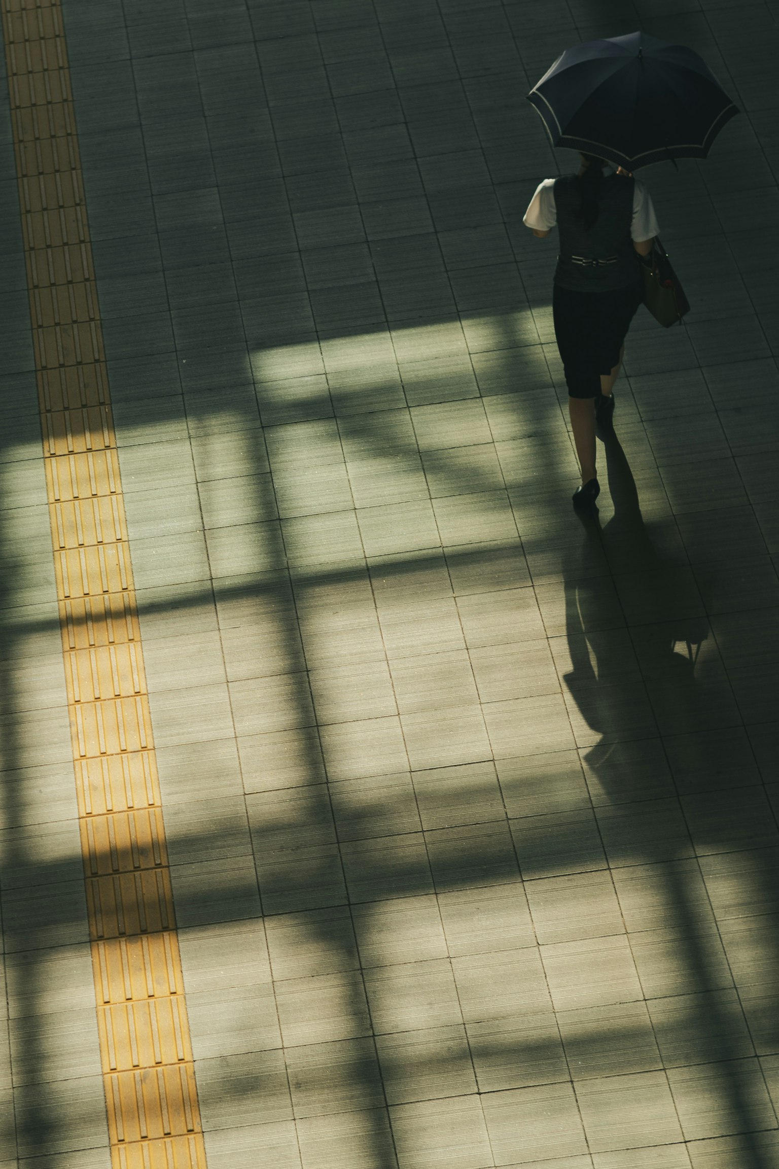 Una persona che cammina con un ombrello proiettando un'ombra sul pavimento di una stazione