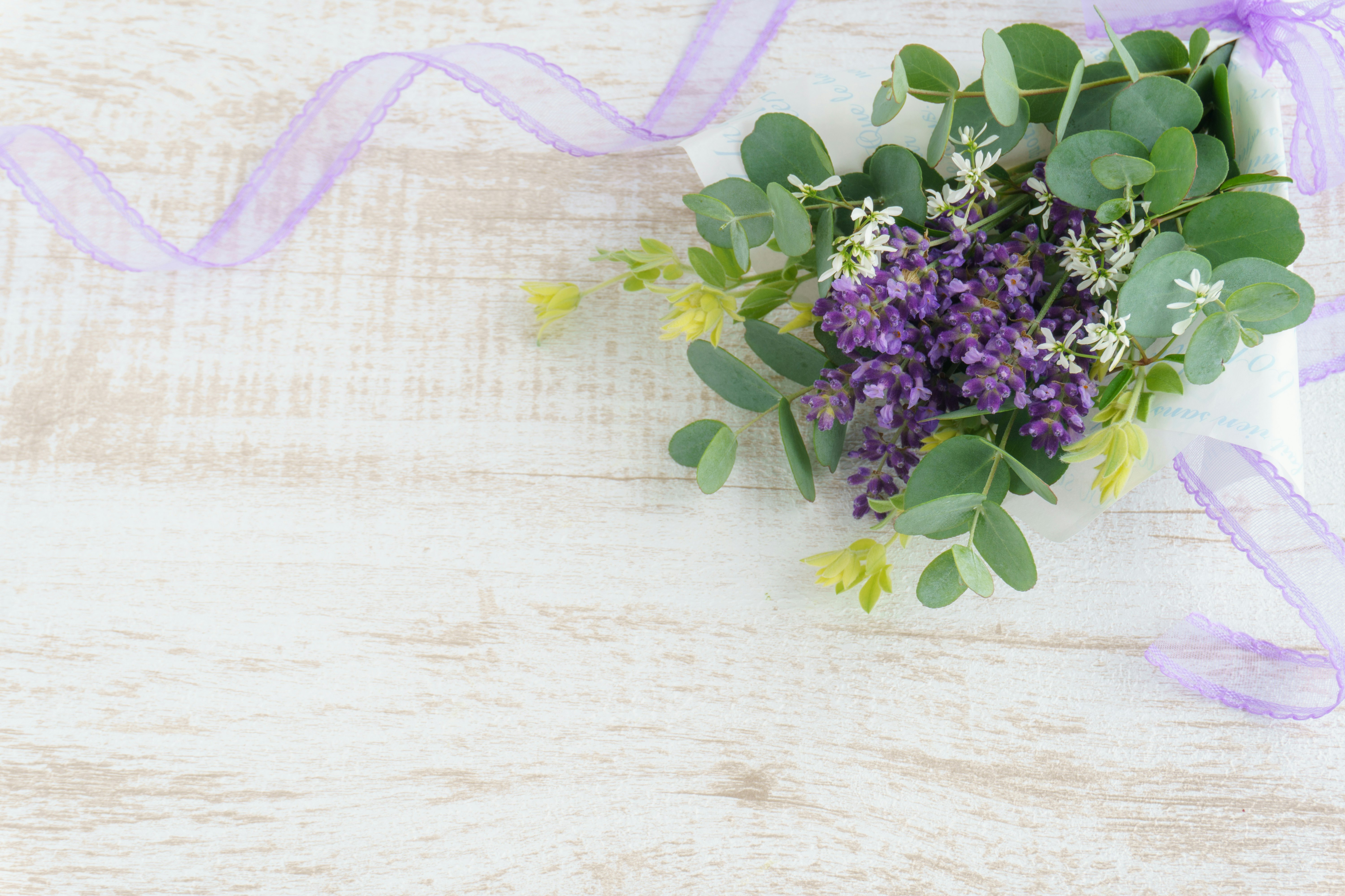 Bouquet di fiori viola e foglie verdi con un nastro viola su una superficie di legno