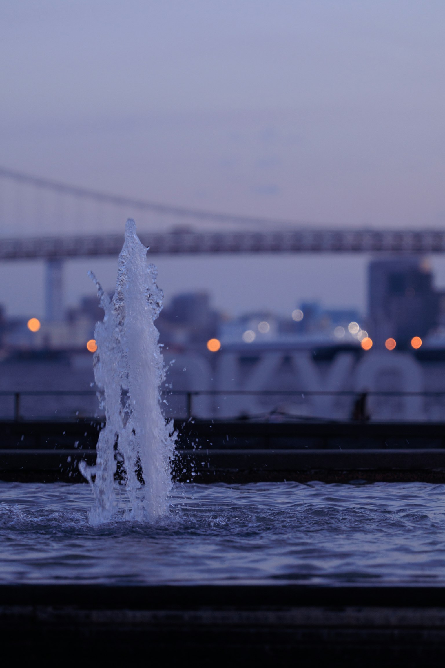 Fountain spraying water at dusk with a bridge in the background