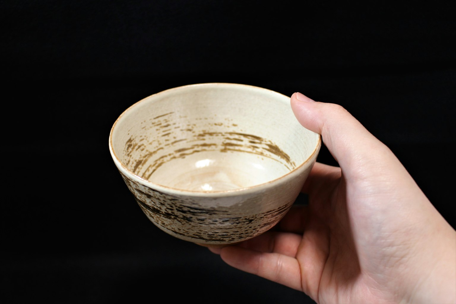 검은 배경에 갈색 무늬가 있는 흰색 도자기 그릇을 들고 있는 손