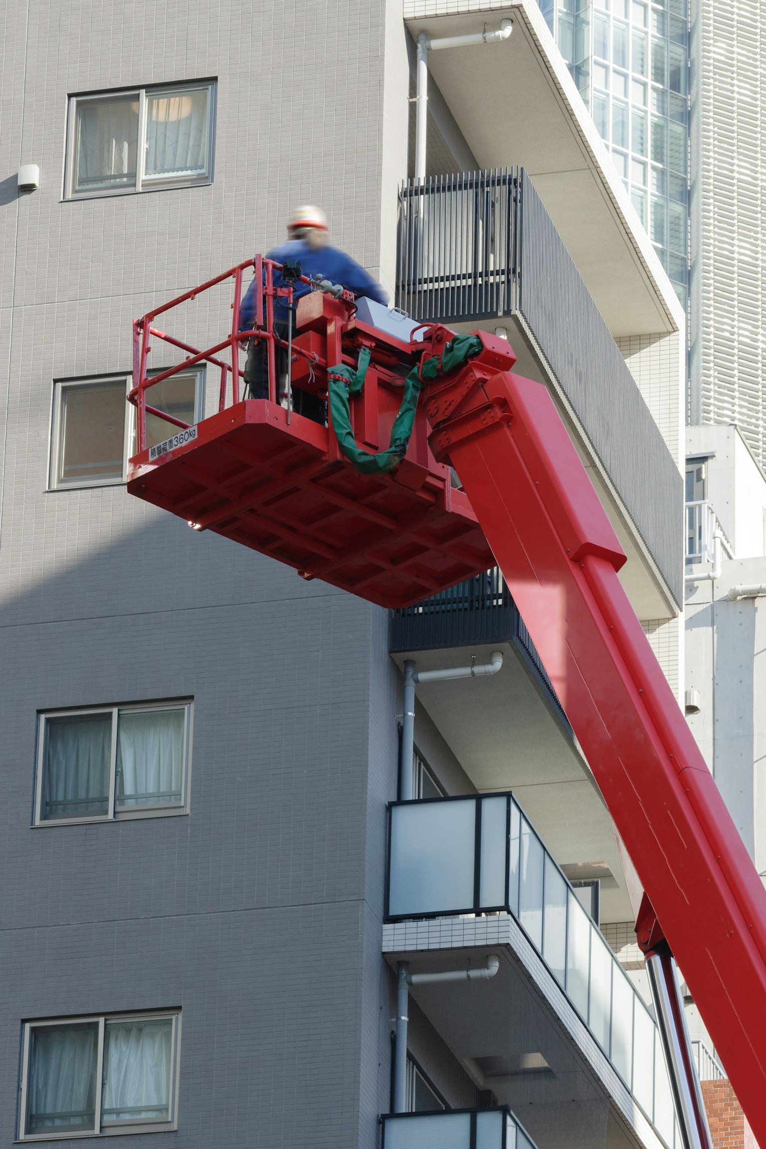 Seorang pekerja di crane merah sedang bekerja di eksterior gedung tinggi