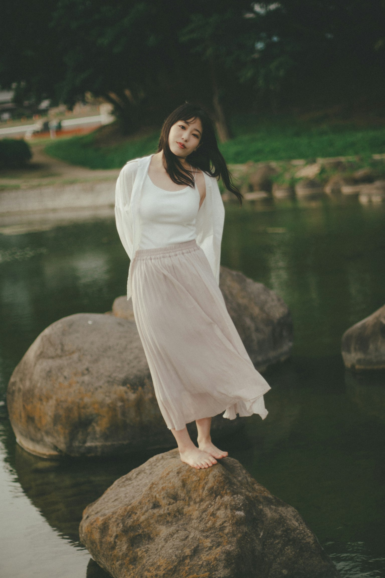 Una donna in piedi su una grande roccia vicino al fiume con un top bianco e una gonna